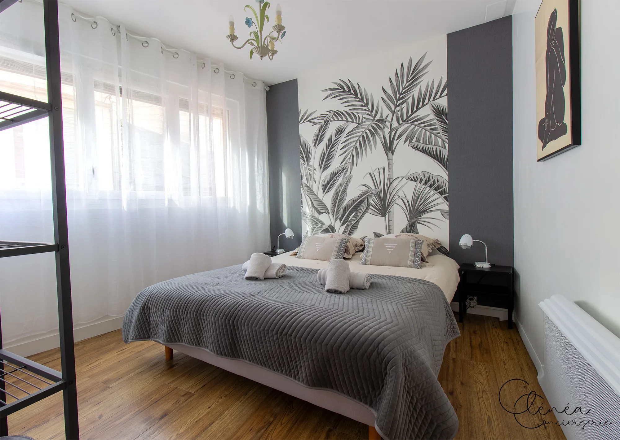 Au Cœur des Lices — Chambre au lit double, tête de lit habillée d'un papier peint tropical, devant une fenêtre voilée.