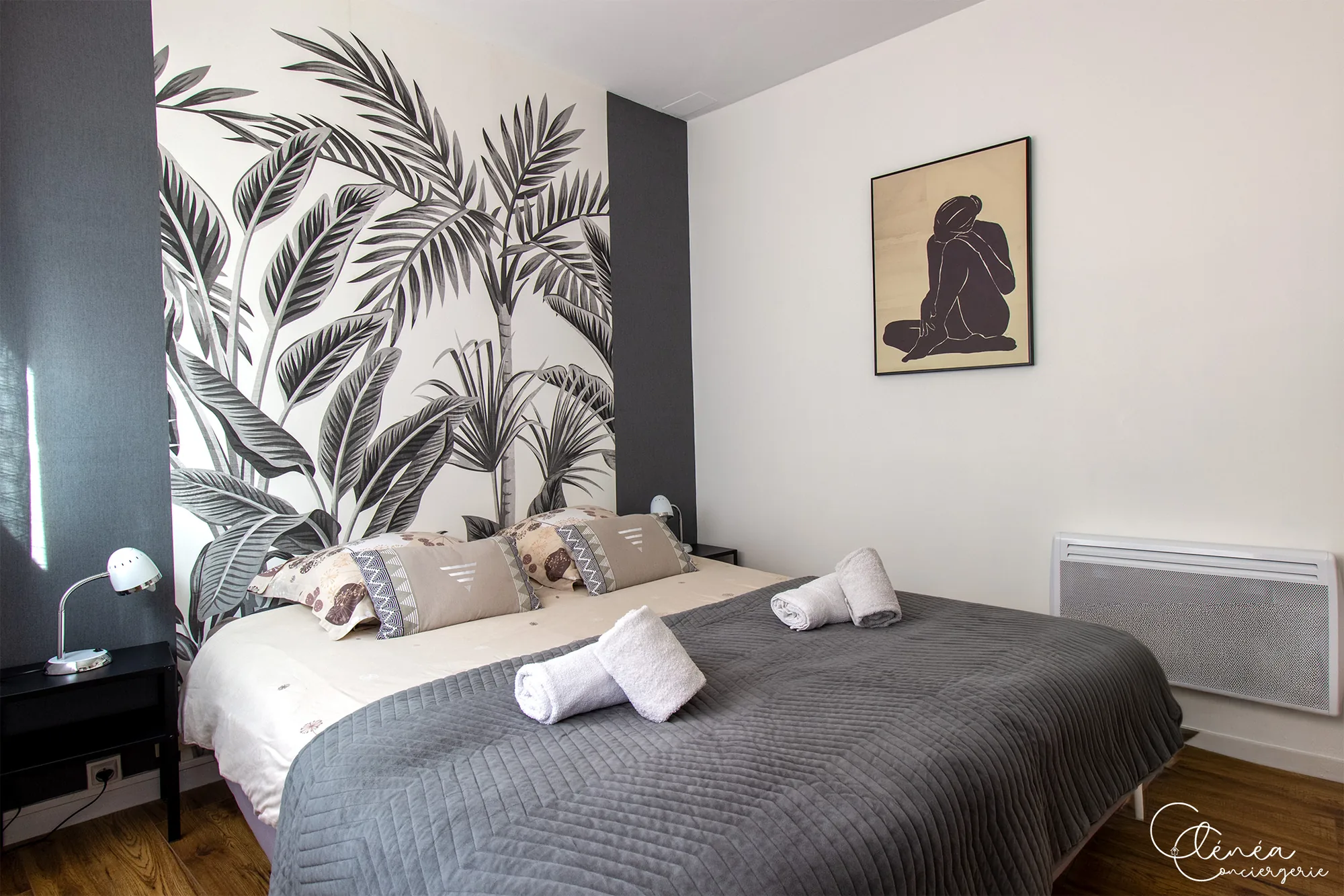 Au Cœur des Lices — La chambre au lit double vue de biais, avec ses deux liseuses et son papier peint à motif de palmiers.