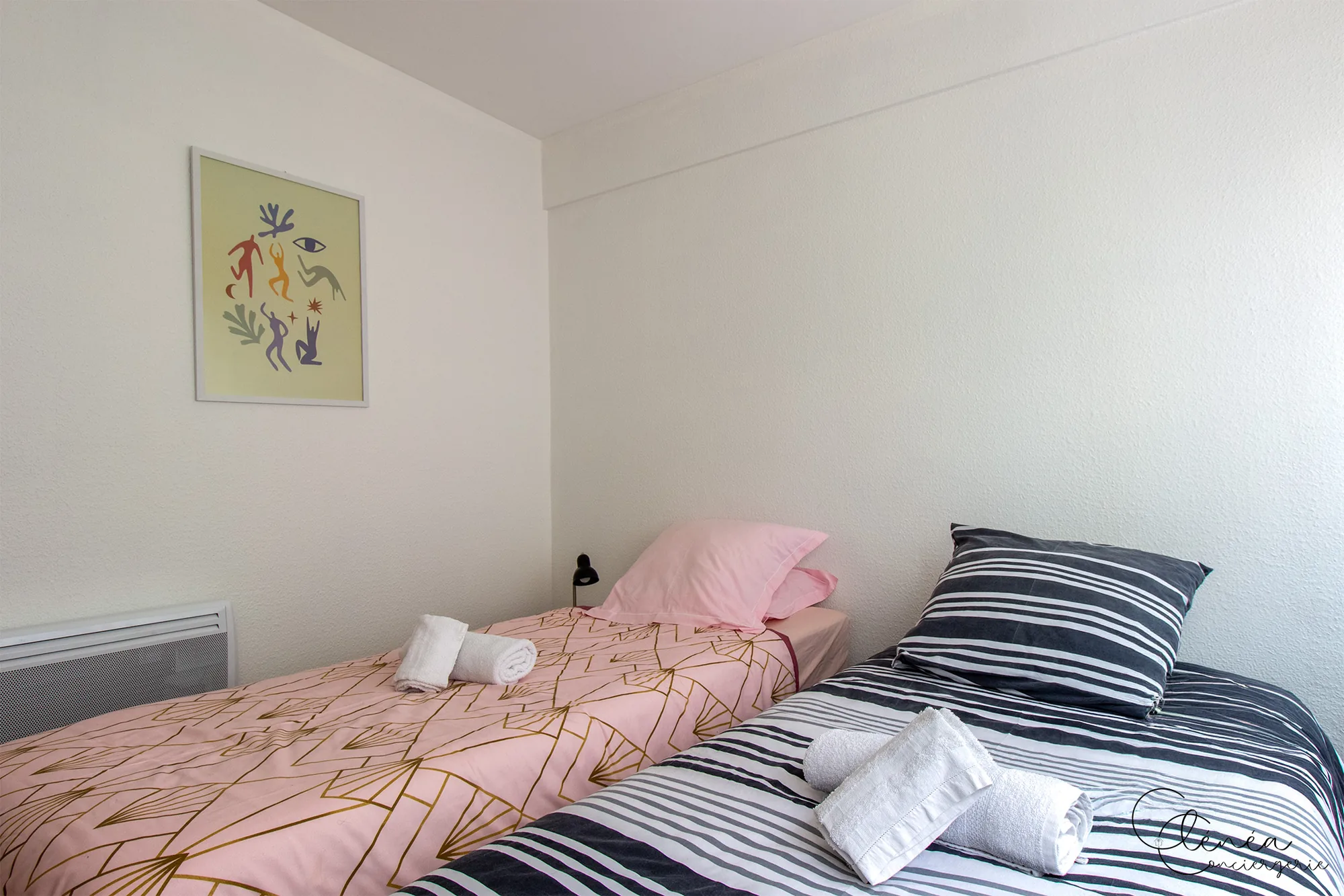Au Cœur des Lices — Chambre aux deux lits simples habillés de linge rose et rayé, sous une affiche colorée.