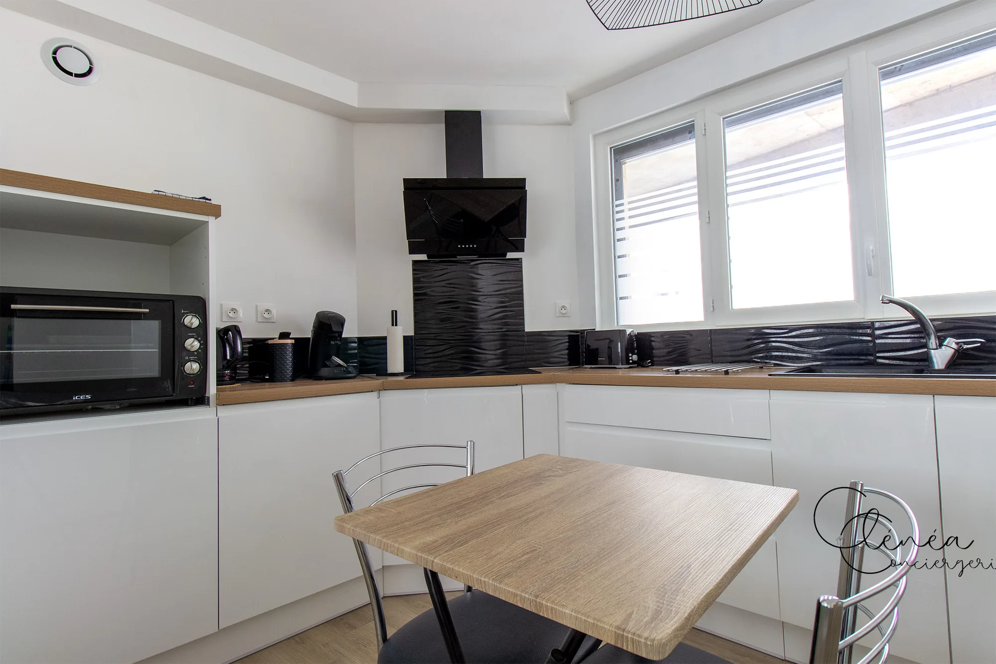 Au Cœur des Lices — La cuisine et sa petite table repas, avec four, cafetière et grille-pain sur le plan de travail.