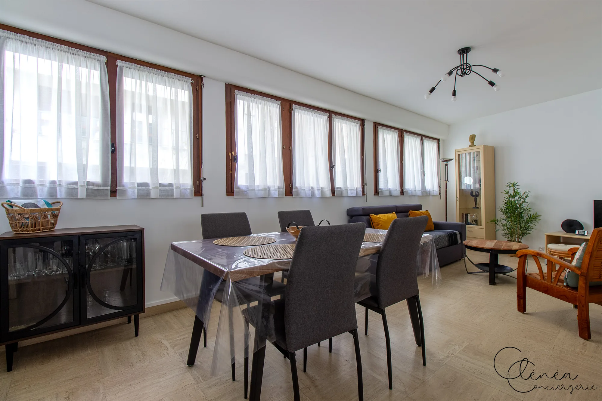 Au Cœur des Lices — Table repas de six couverts dans le séjour, devant le canapé et le fauteuil en bois.
