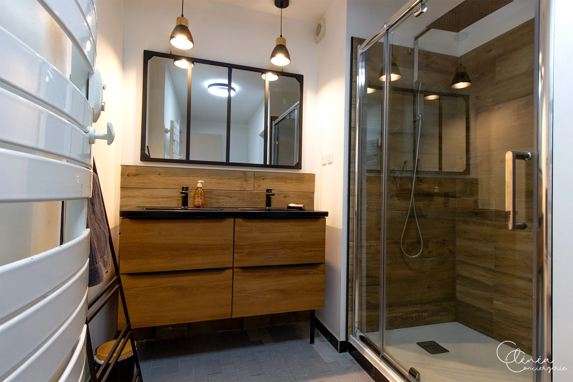 Au Cœur des Lices — Salle de bain avec double vasque noire, grand miroir et cabine de douche.