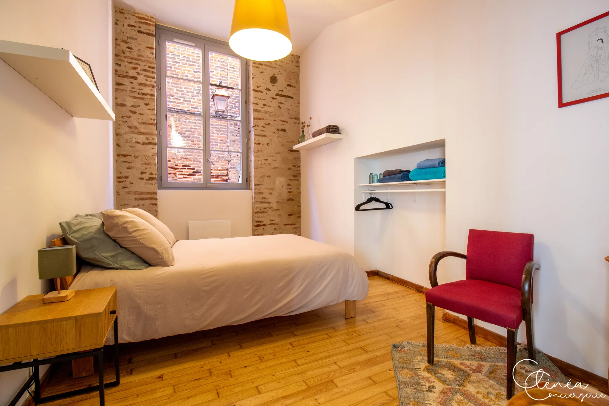 Chez Ludi et Pierre — Chambre avec lit double, fenêtre encadrée de briques apparentes, niche penderie et fauteuil rouge
