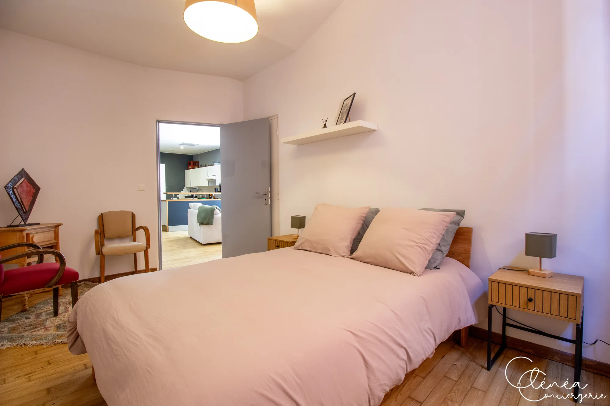 Chez Ludi et Pierre — Lit double de la chambre 2, tables de chevet et porte ouverte sur la pièce de vie et la cuisine