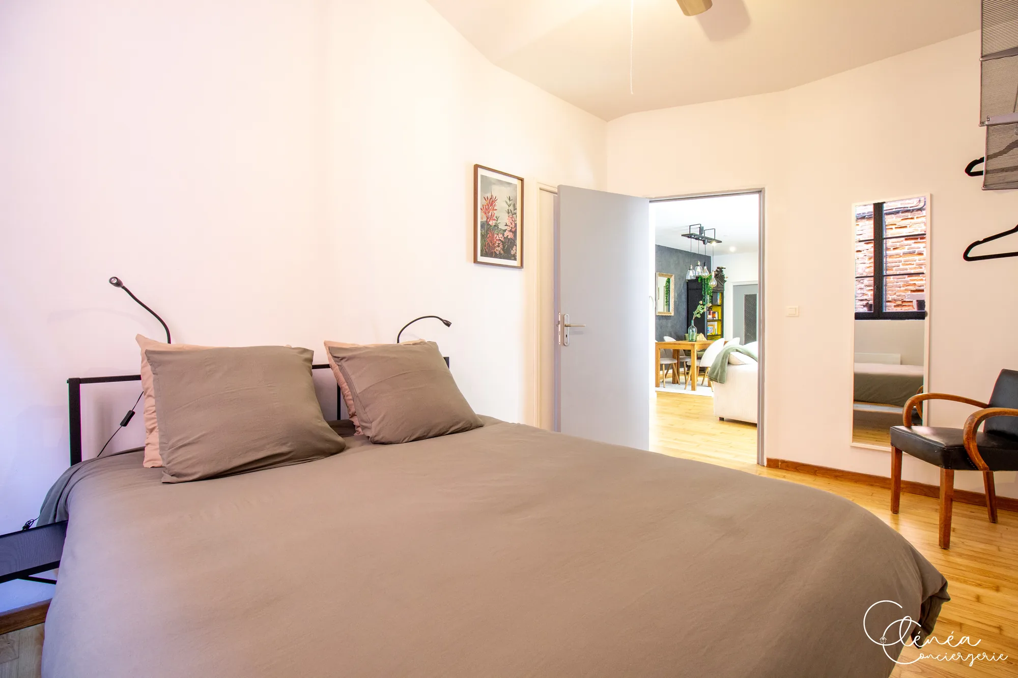 Chez Ludi et Pierre — Lit de la chambre 1 avec deux liseuses, miroir et porte ouverte sur la pièce de vie