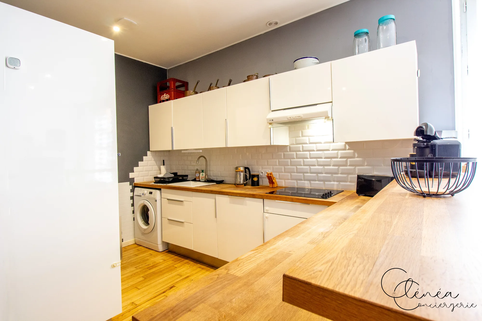 Chez Ludi et Pierre — Cuisine avec plan de travail en bois, crédence en carreaux métro, plaque vitrocéramique, hotte et lave-linge
