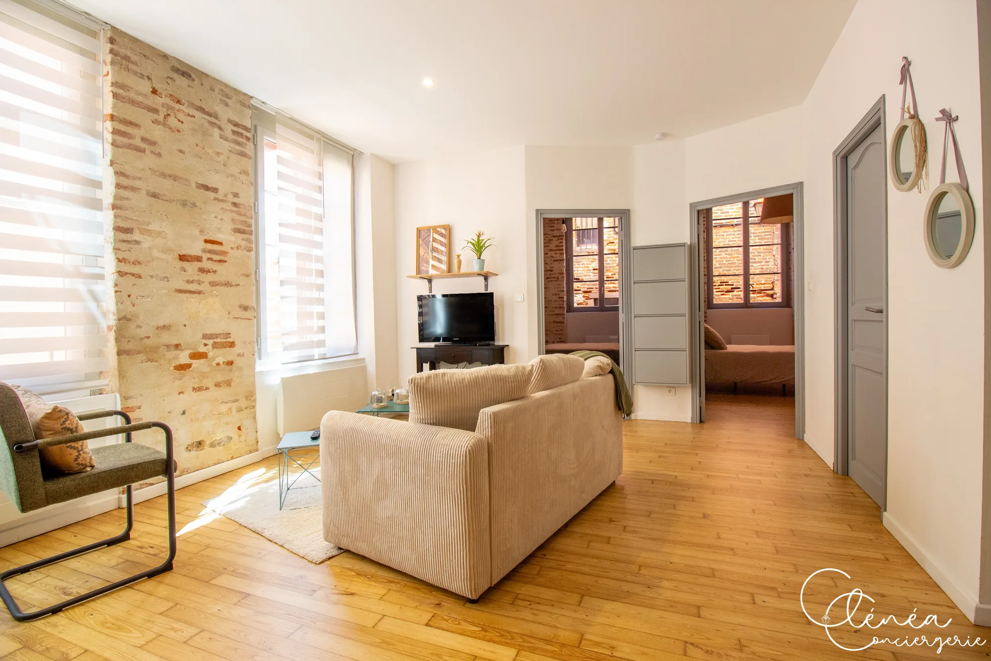 Chez Ludi et Pierre — Salon avec canapé et télévision devant un mur de briques, et les portes ouvertes sur les deux chambres