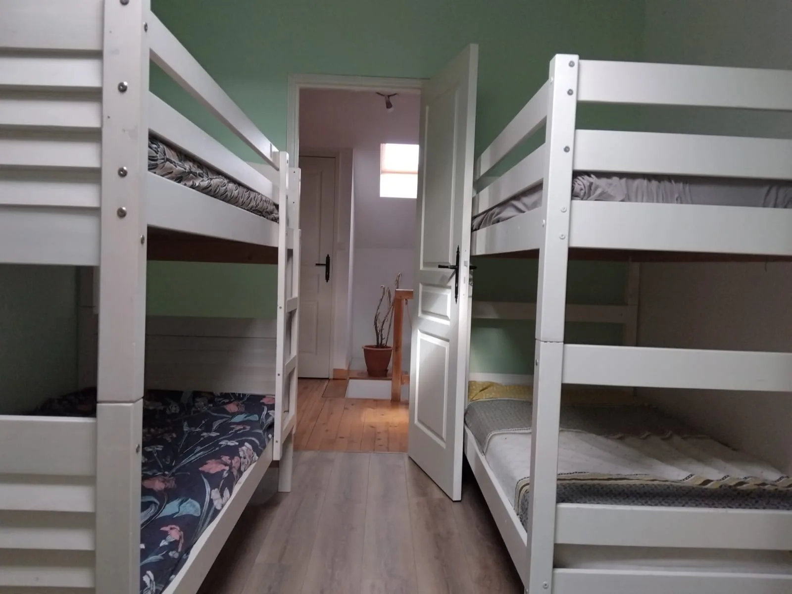 L’Escapade Albigeoise — Chambre mansardée aux murs verts avec deux lits superposés en bois blanc de part et d’autre du passage