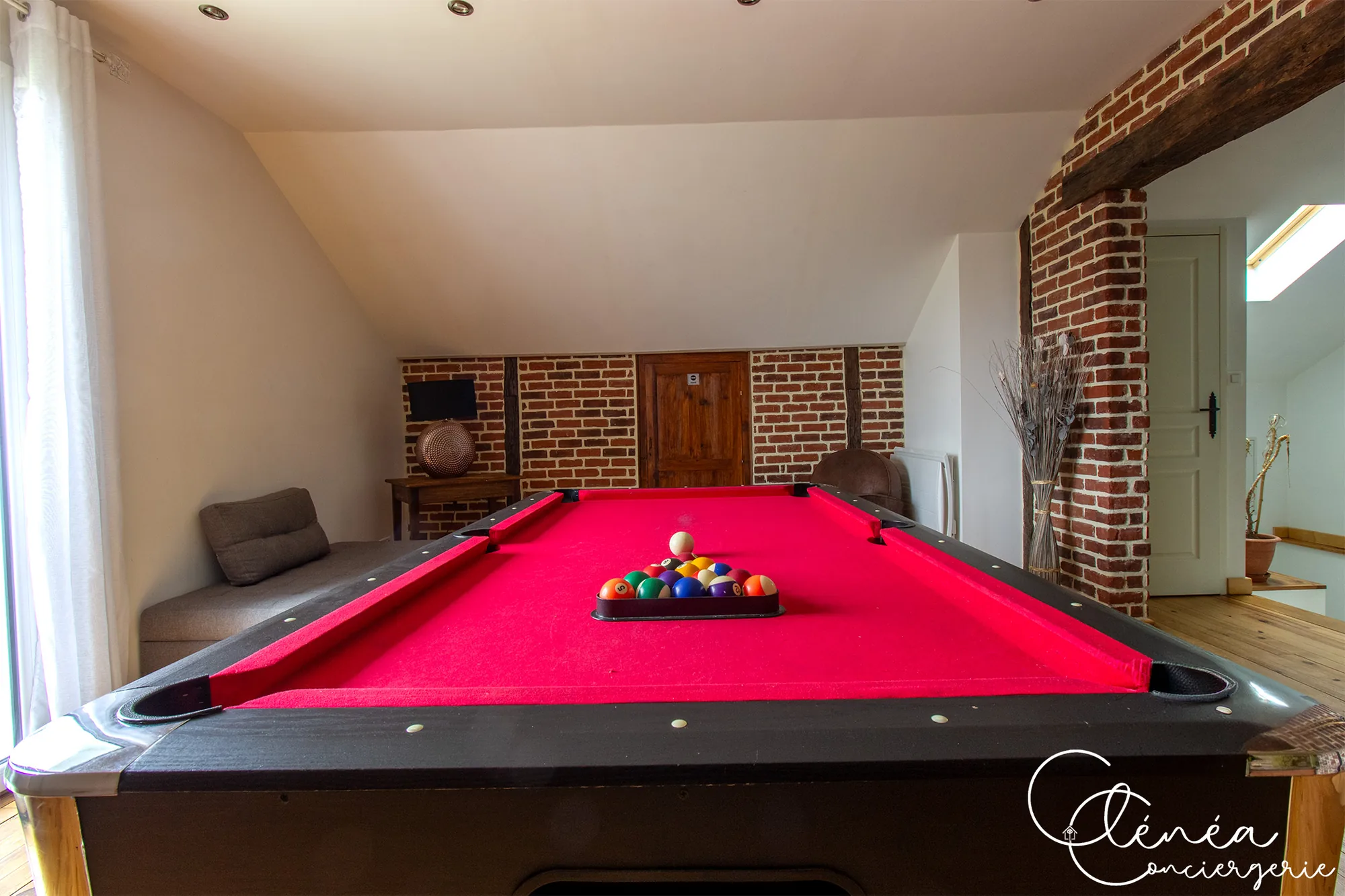 L’Escapade Albigeoise — Billard américain prêt à jouer, avec une banquette grise et une console en bois le long du mur de briques
