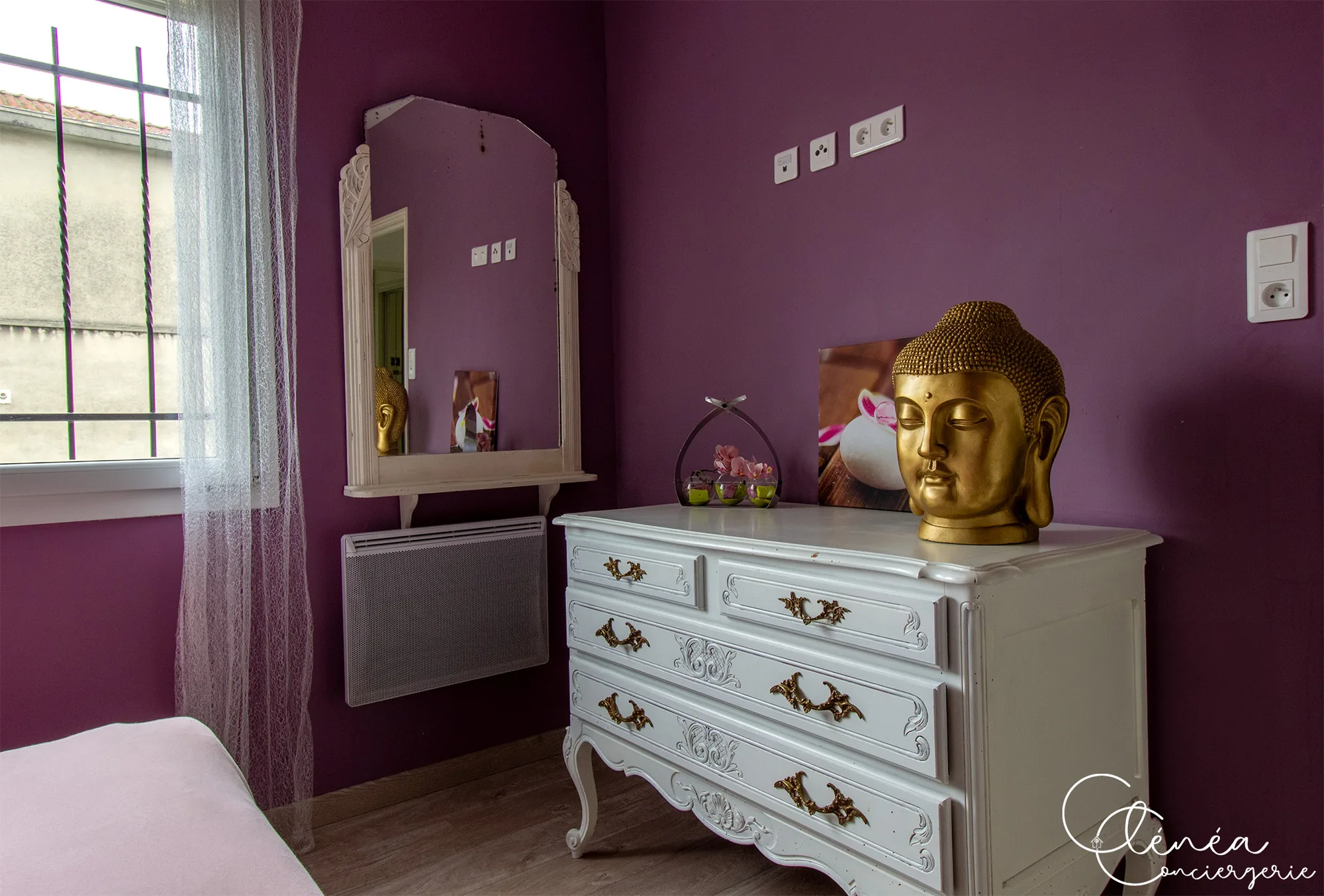 L’Escapade Albigeoise — Commode blanche patinée surmontée d’une tête de Bouddha dorée, à côté d’un miroir mural dans la chambre violette