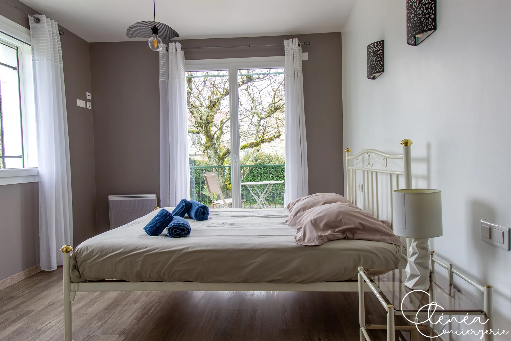 L’Escapade Albigeoise — Chambre aux murs taupe avec lit en fer forgé blanc et porte-fenêtre ouvrant sur un petit espace extérieur