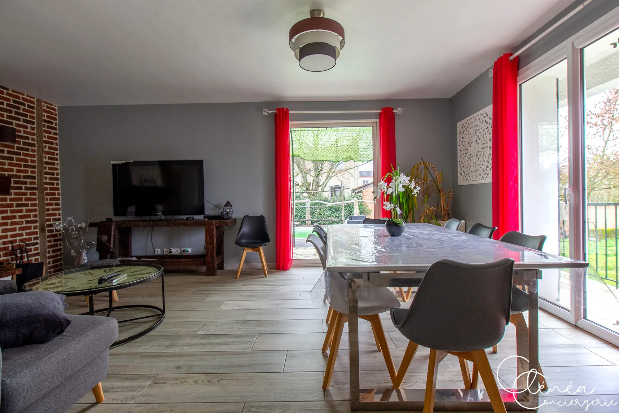 L’Escapade Albigeoise — Pièce de vie avec grande table à manger, chaises, télévision et baies vitrées ouvertes sur le jardin