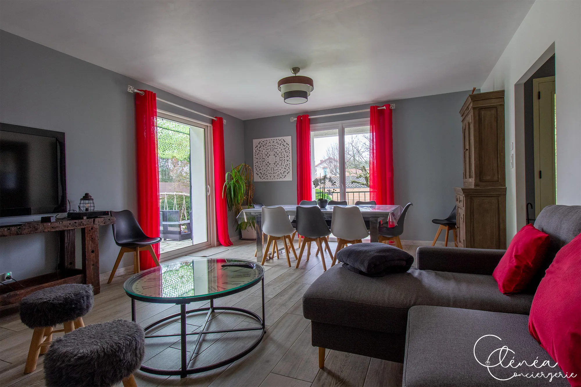 L’Escapade Albigeoise — Salon avec canapé gris, table basse ronde et coin repas devant les baies vitrées