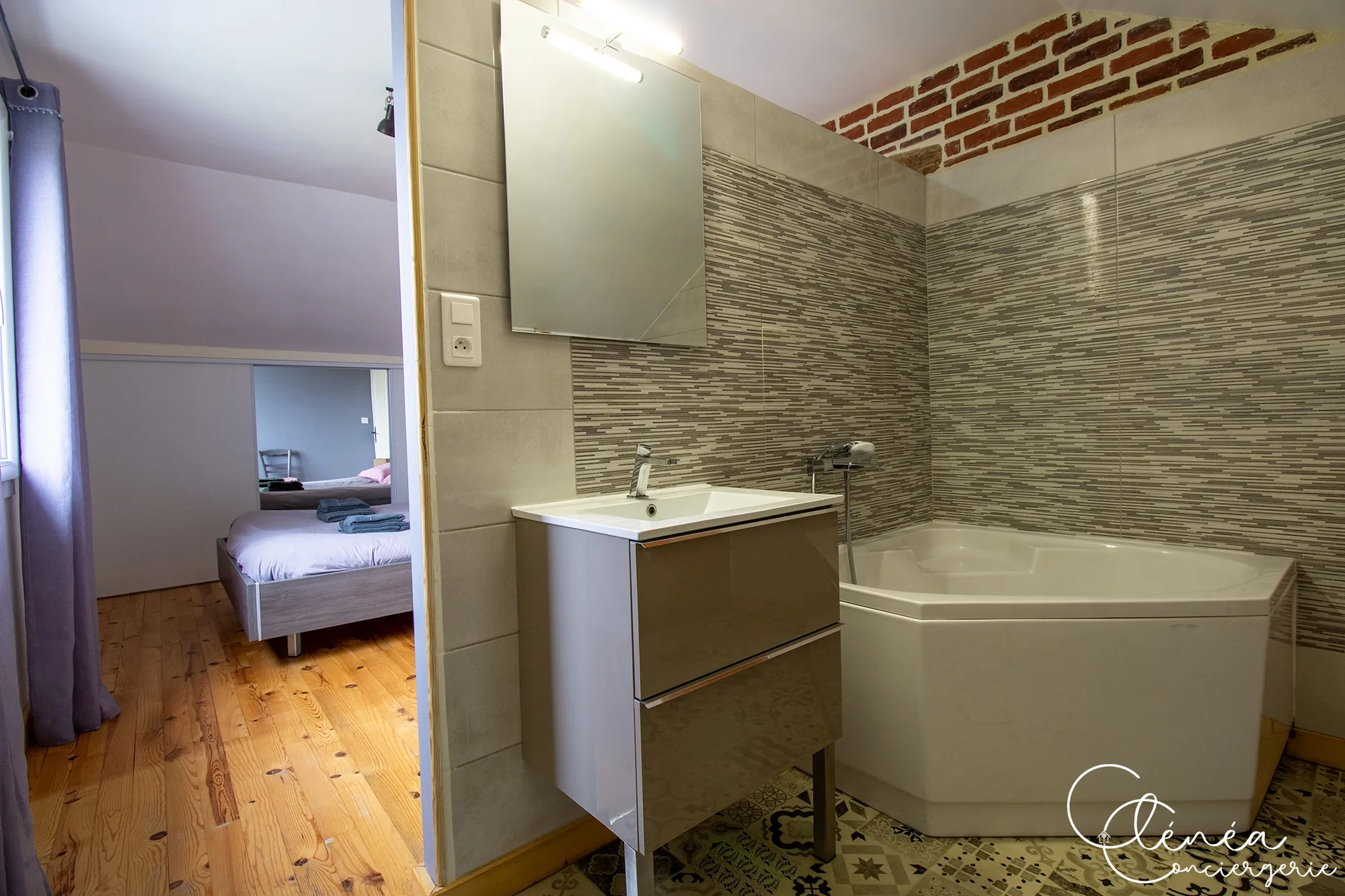 L’Escapade Albigeoise — Salle d’eau ouverte sur la chambre, avec baignoire d’angle, meuble vasque et sol en carreaux de ciment