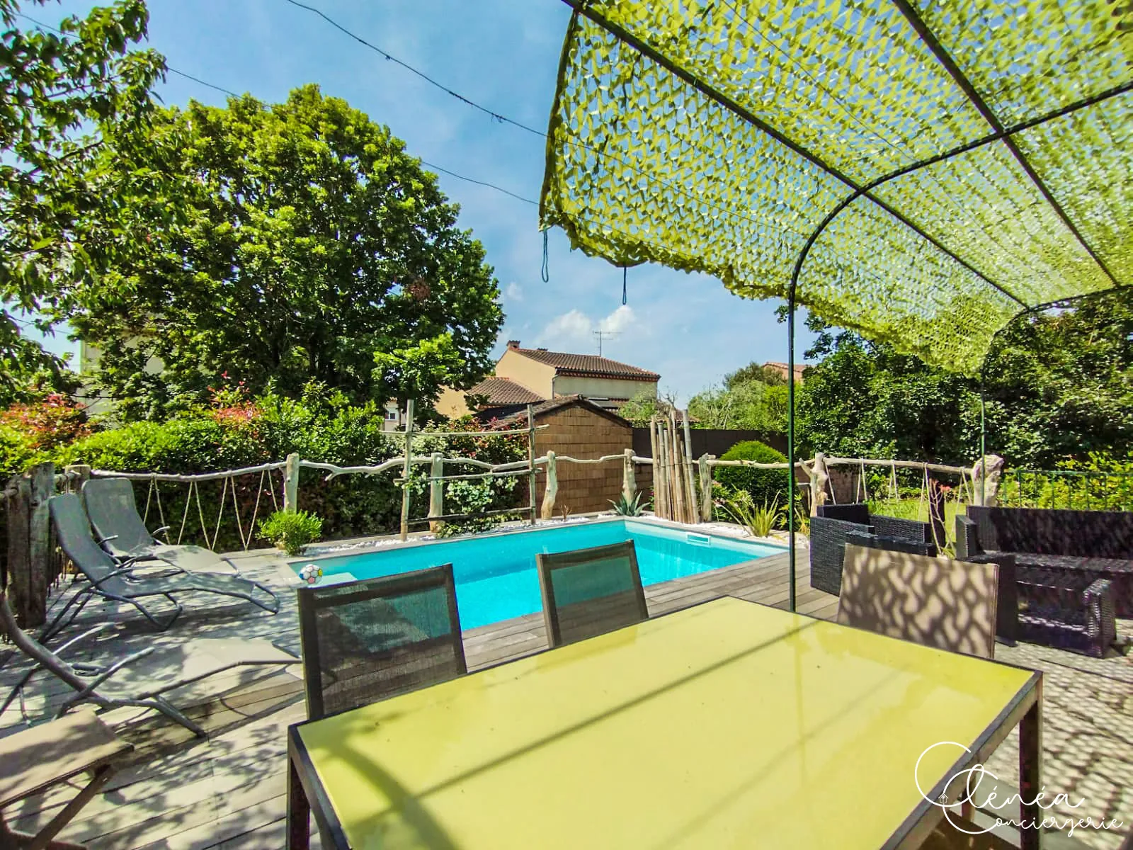 L’Escapade Albigeoise — Terrasse en bois au bord de la piscine, avec transats, table extérieure et voile d’ombrage vert