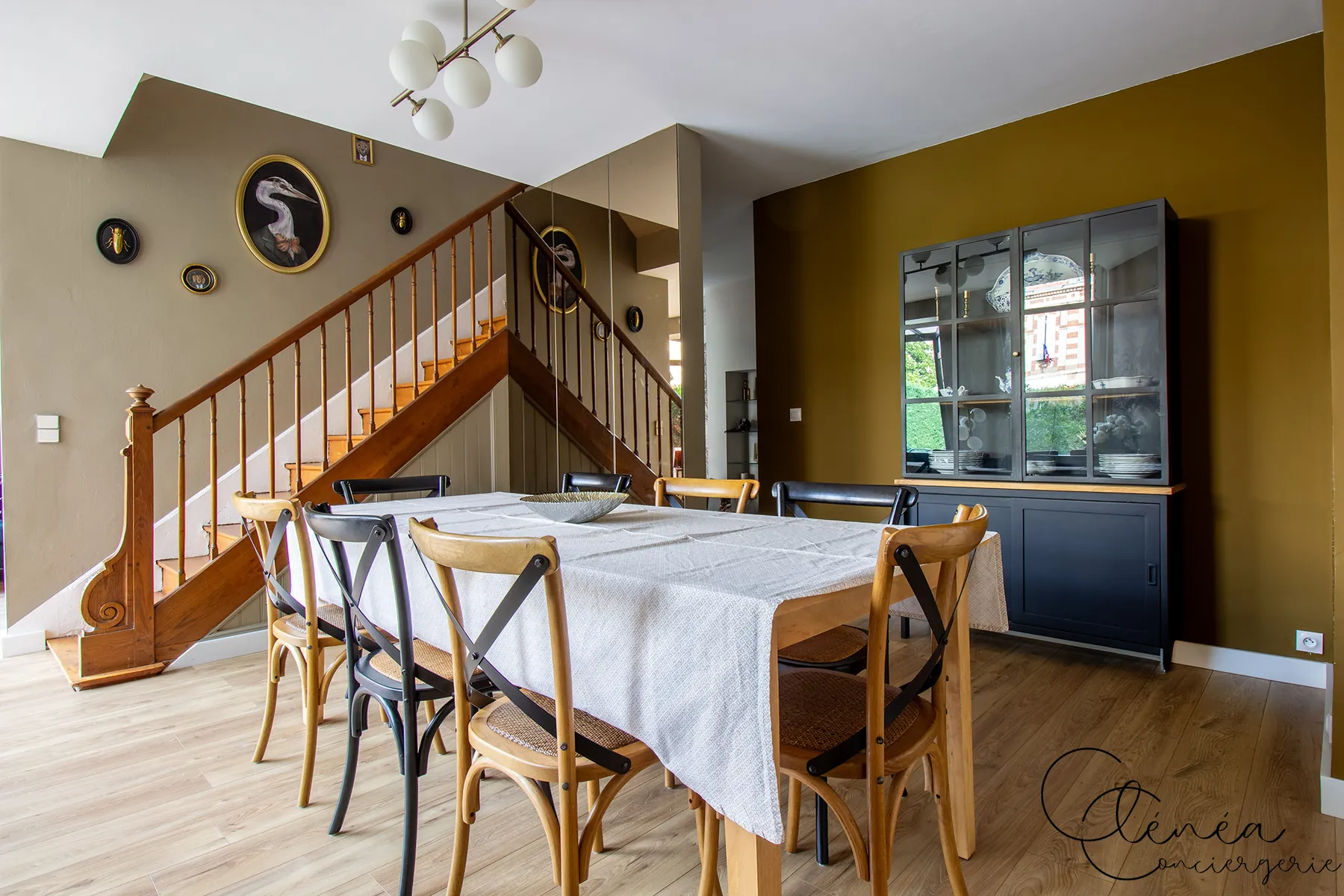 Évasion — Salle à manger avec grande table, vaisselier vitré et escalier en bois