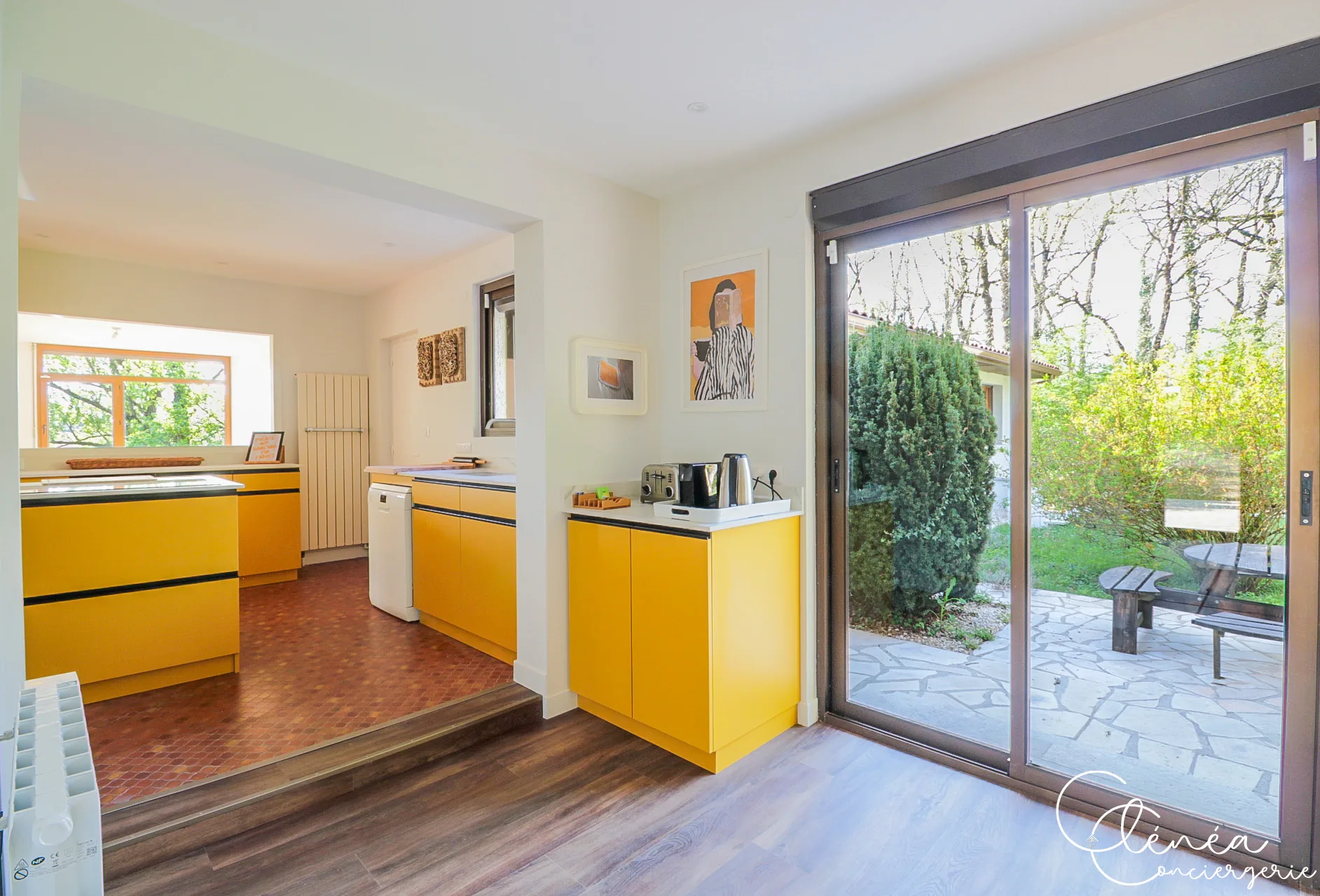 GreenOak — Cuisine aux façades jaunes avec baie vitrée coulissante ouvrant sur une terrasse en pierre et le jardin