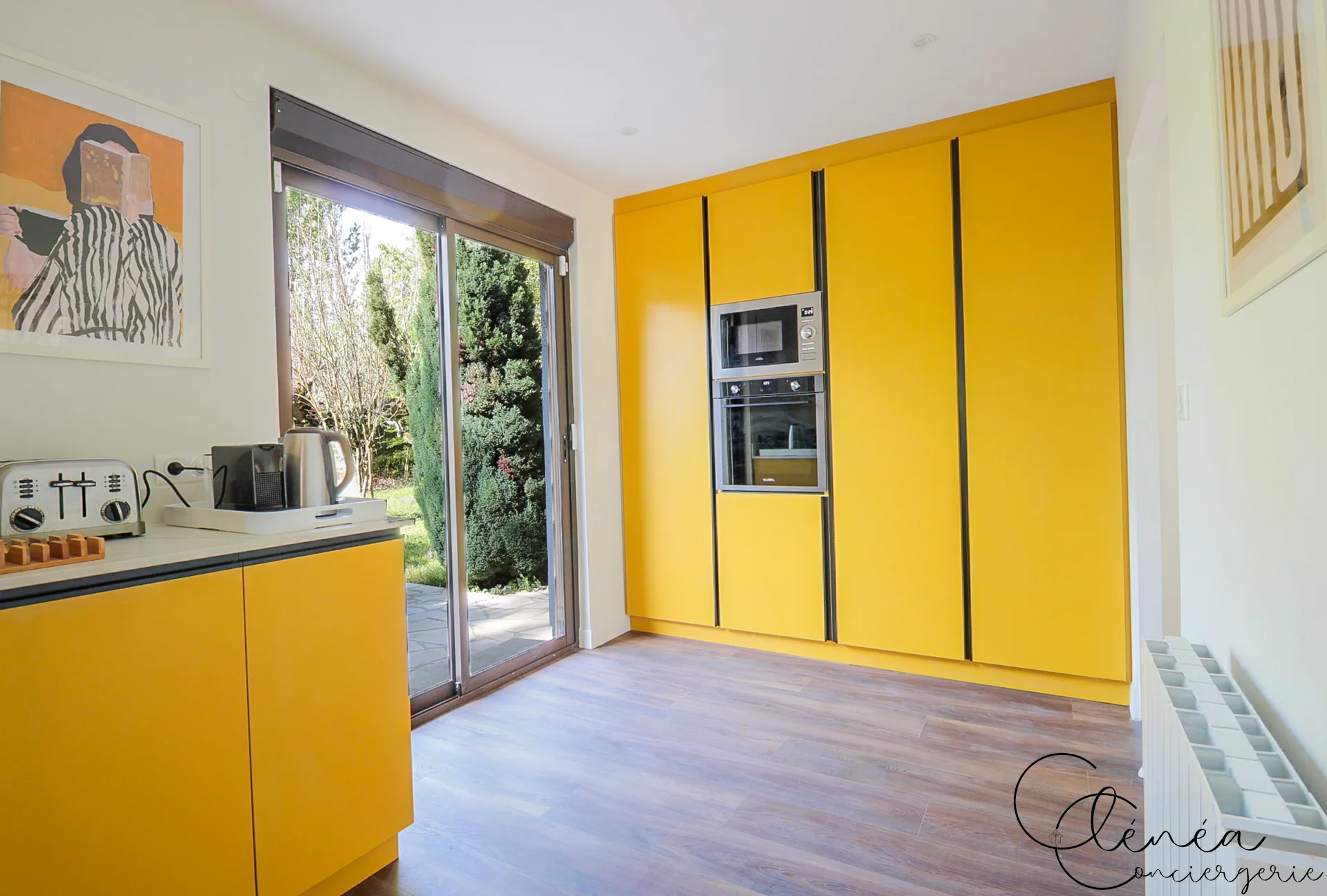 GreenOak — Colonne de rangements jaunes intégrant le four et le micro-ondes, à côté d’une baie vitrée sur le jardin