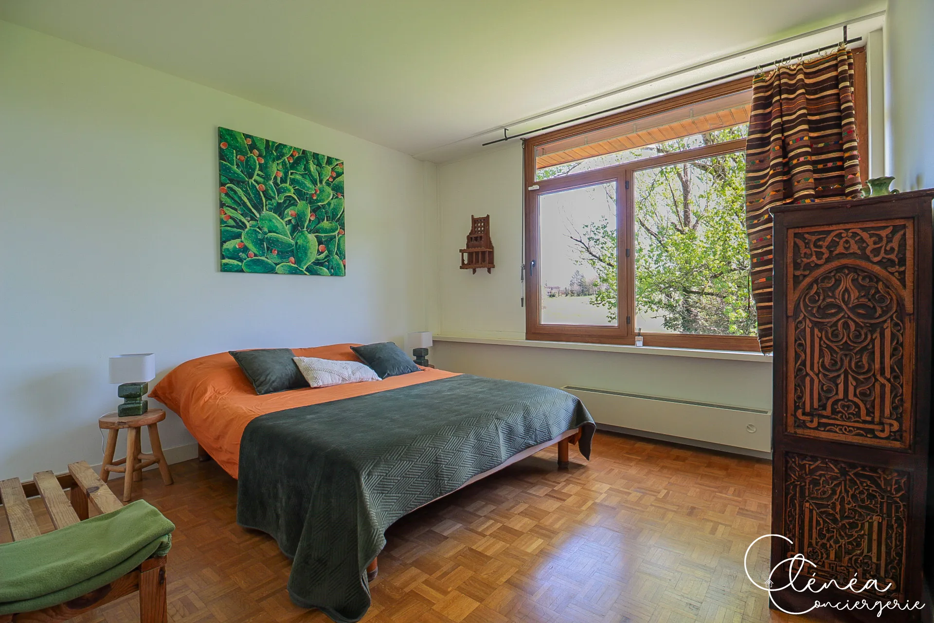 GreenOak — Chambre avec lit double au couvre-lit vert, toile représentant des cactus et armoire en bois sculpté
