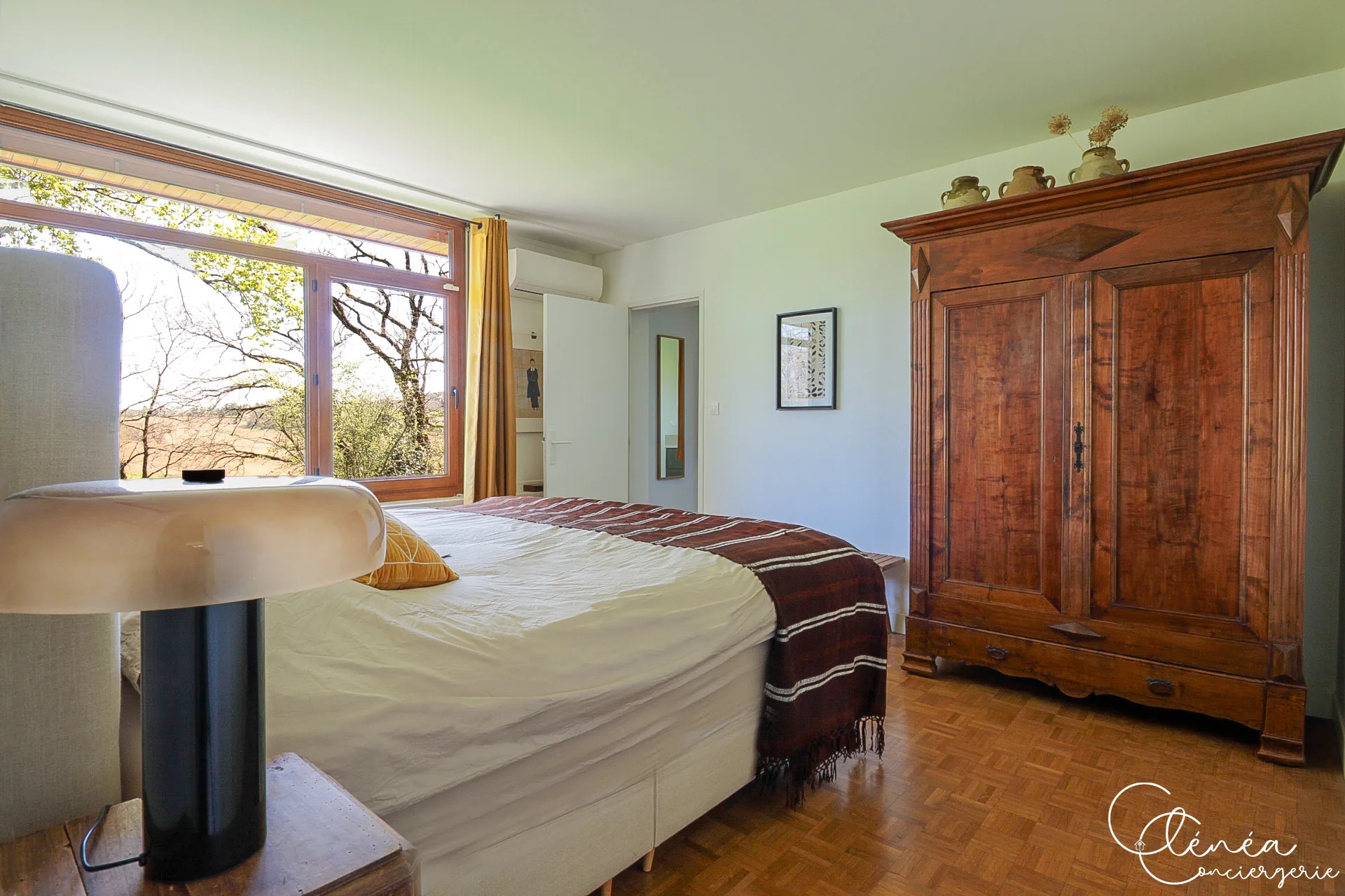 GreenOak — Chambre avec armoire ancienne en bois, climatisation murale et fenêtre ouverte sur la campagne