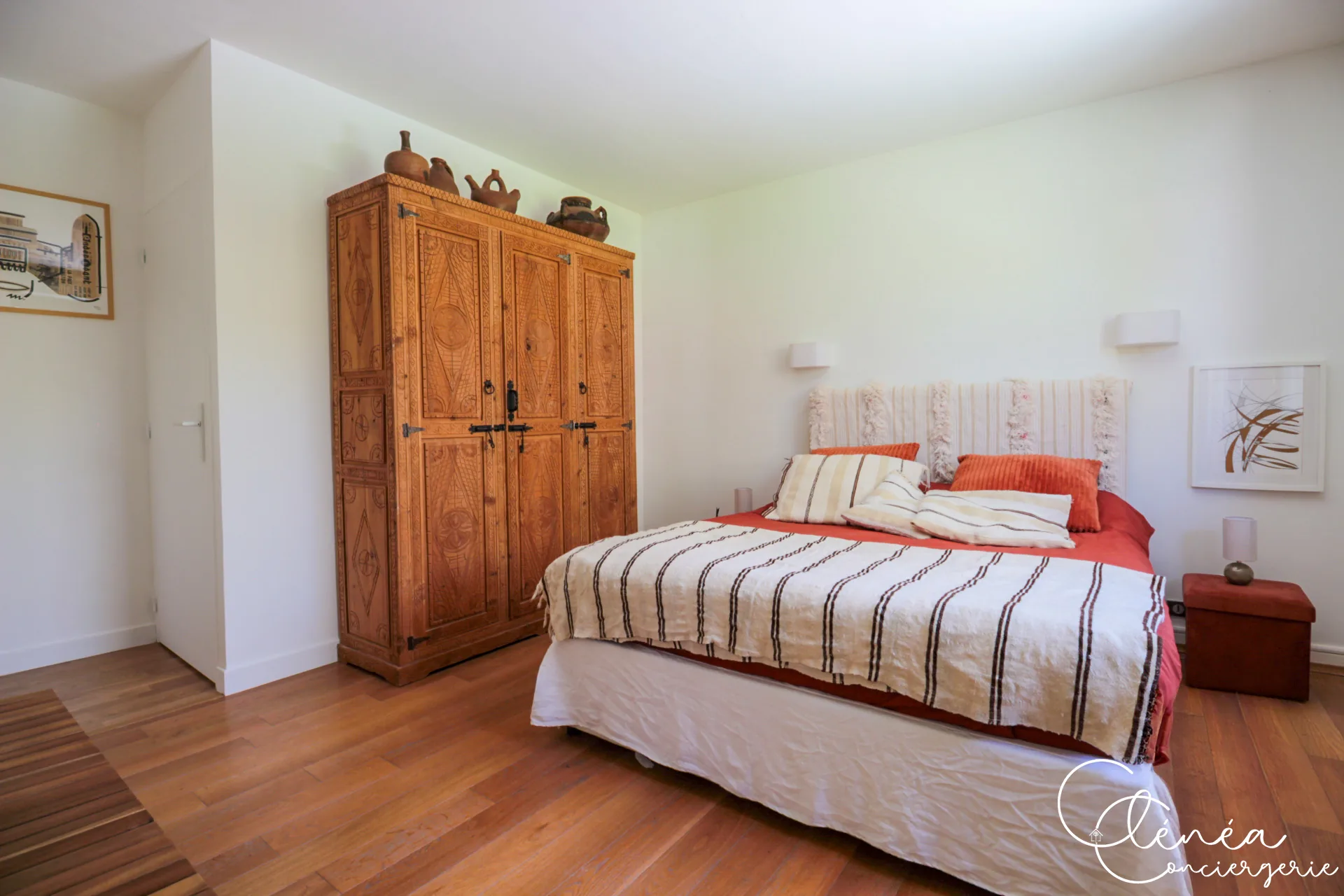 GreenOak — Armoire en bois sculpté et lit double aux textiles rayés dans une chambre au parquet clair