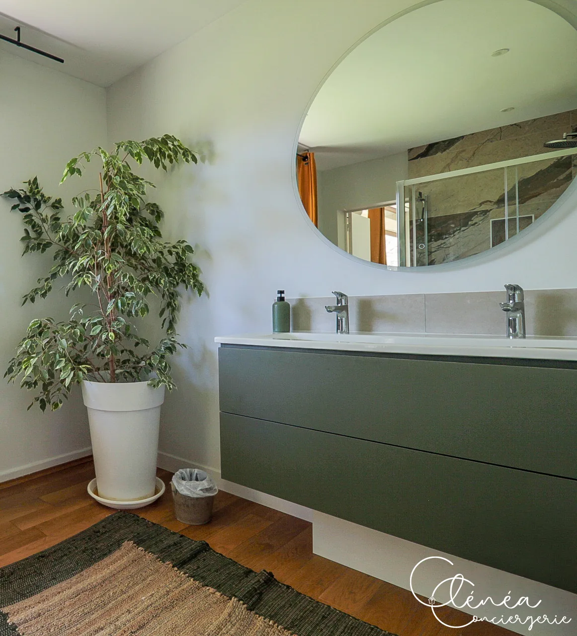 GreenOak — Meuble double vasque vert surmonté d’un grand miroir rond, avec plante verte et tapis