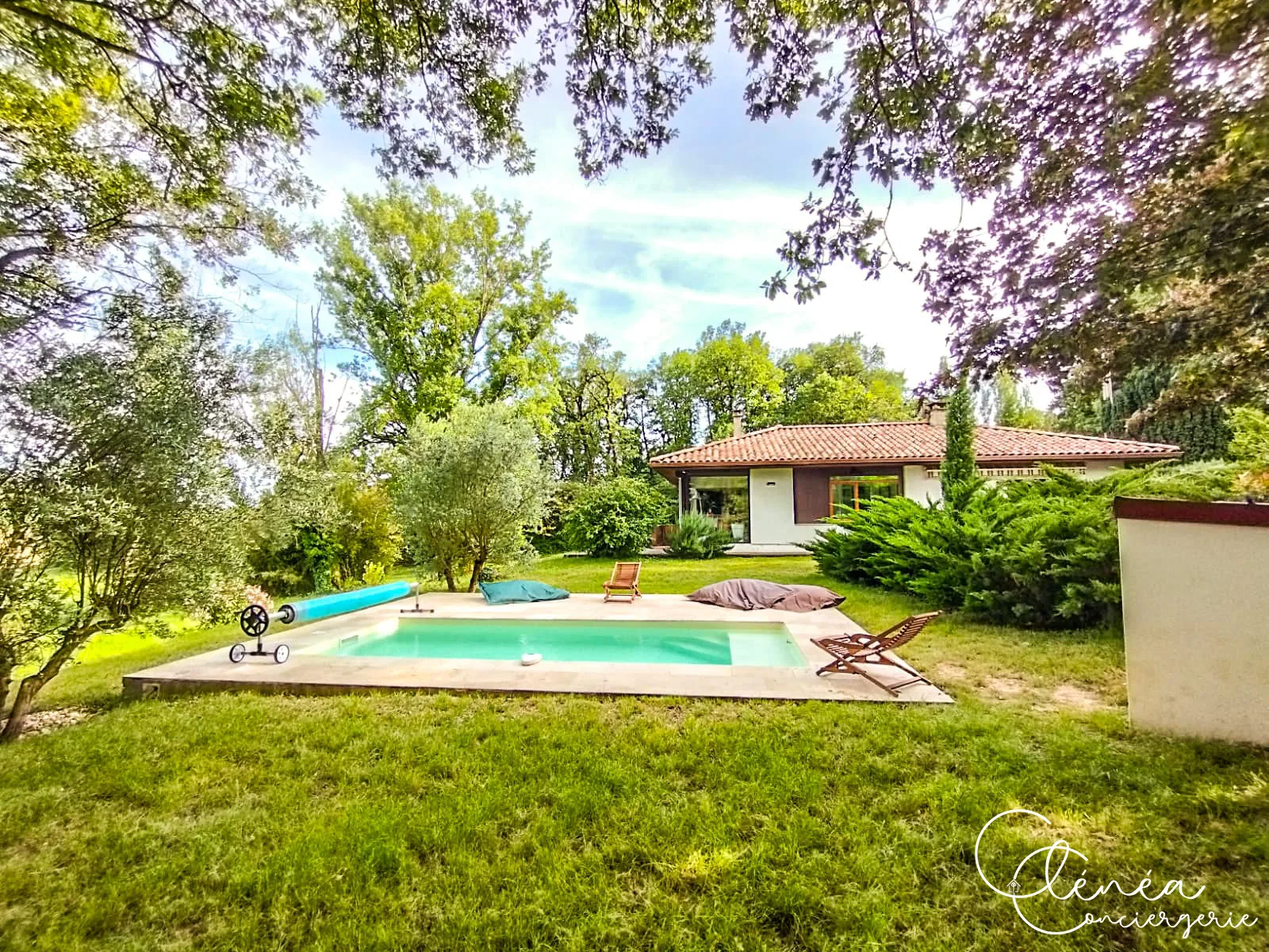 GreenOak — Piscine bordée d’une plage en pierre au milieu du jardin arboré, la maison en arrière-plan