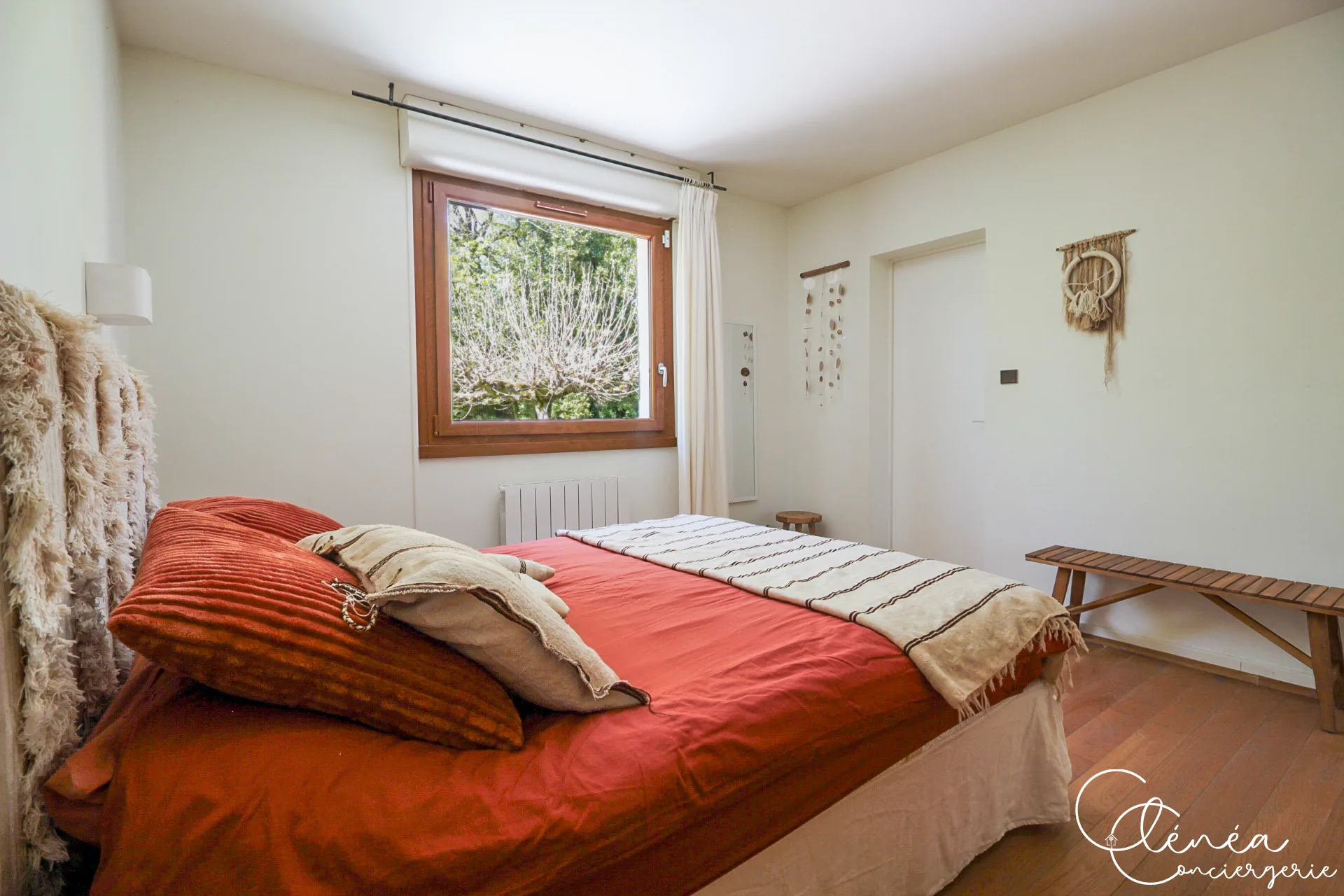 GreenOak — Chambre au lit habillé de rouge, banc en bois le long du mur et fenêtre sur le jardin