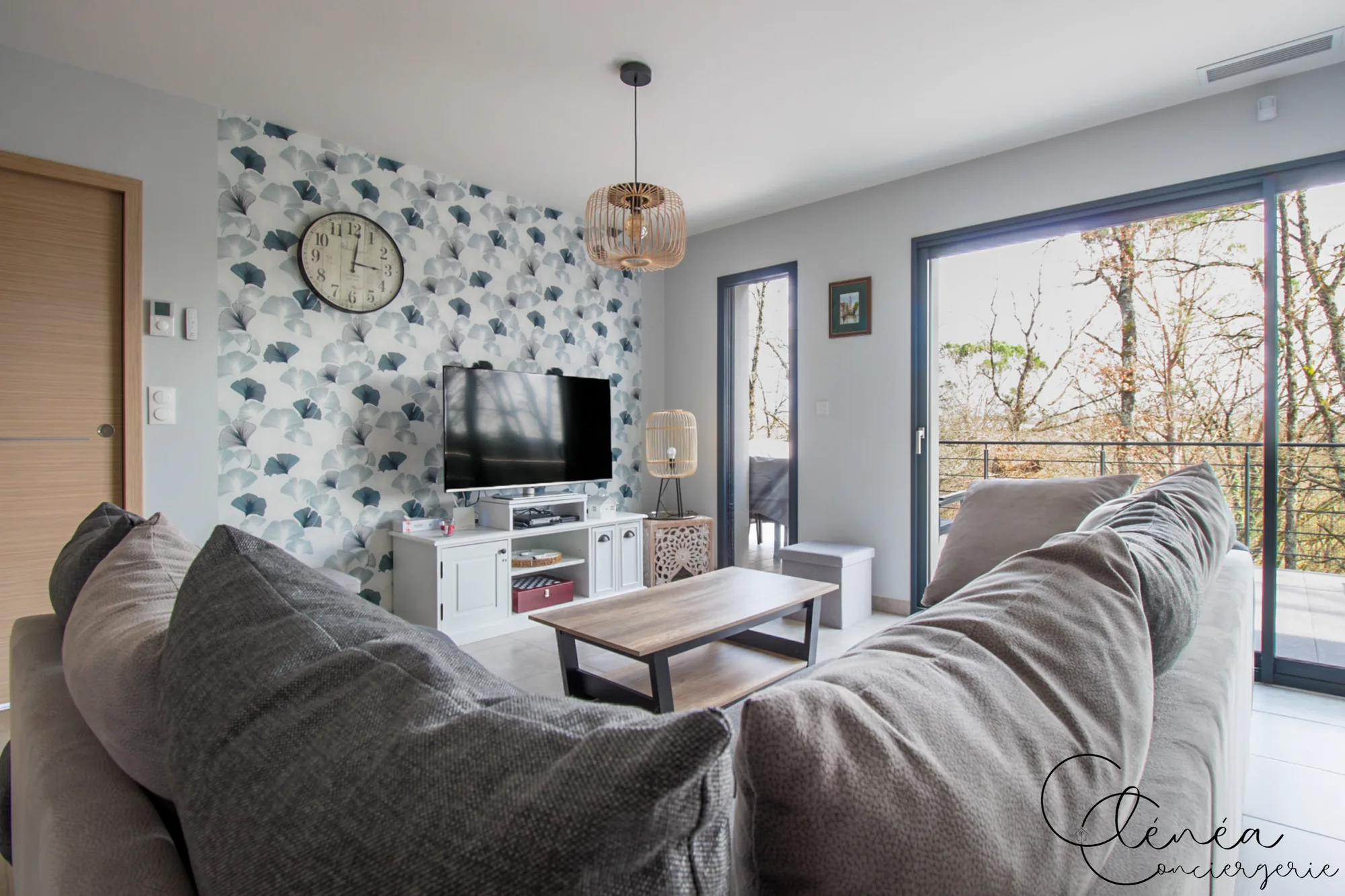 La Vigne — Coin télévision du salon devant le mur au papier peint ginkgo, avec table basse en bois.