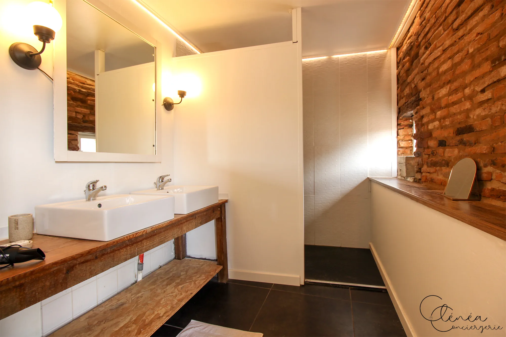 Le Quinze — Salle de bain avec double vasque posée sur un plan en bois, miroir et mur de briques apparentes