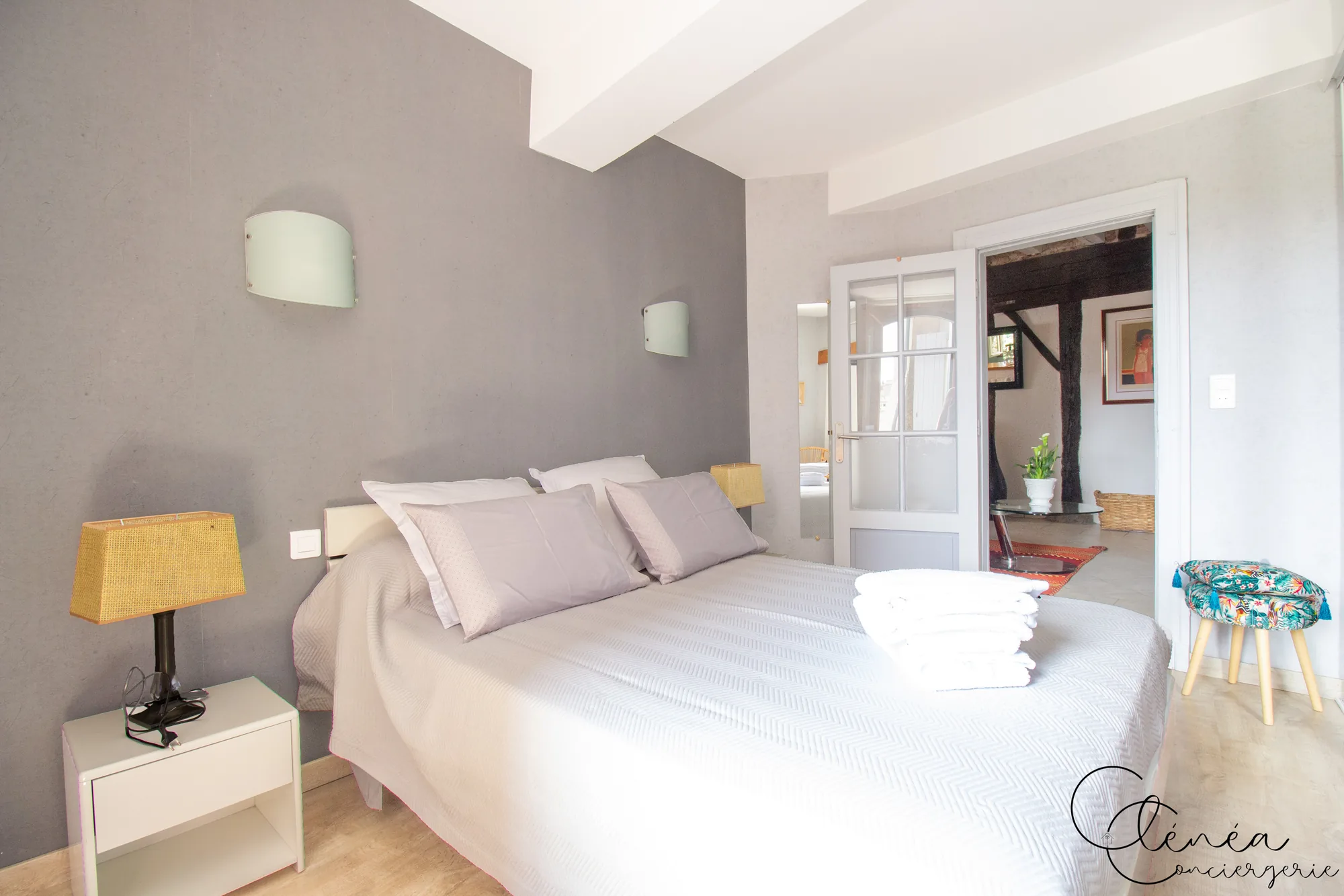Saudade d’Albi — Chambre aux murs gris avec lit double préparé, serviettes pliées, table de chevet et porte vitrée ouverte sur la pièce de vie.