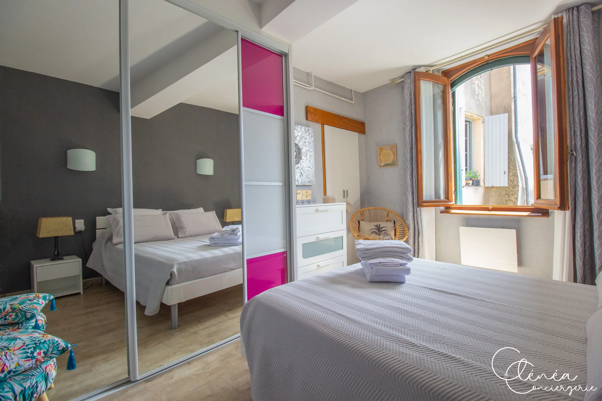 Saudade d’Albi — Chambre avec placard à portes coulissantes miroir, commode blanche, fauteuil en rotin et fenêtre ouverte sur une ruelle.