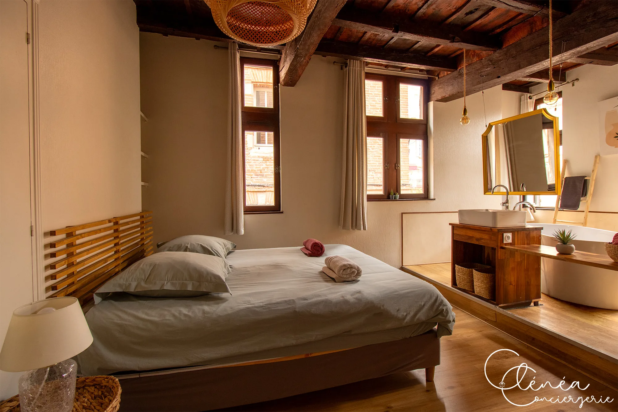 Sous les Toits de Sainte Cécile — Chambre sous plafond à poutres avec lit double, tête de lit en lattes de bois et salle de bain ouverte sur une estrade