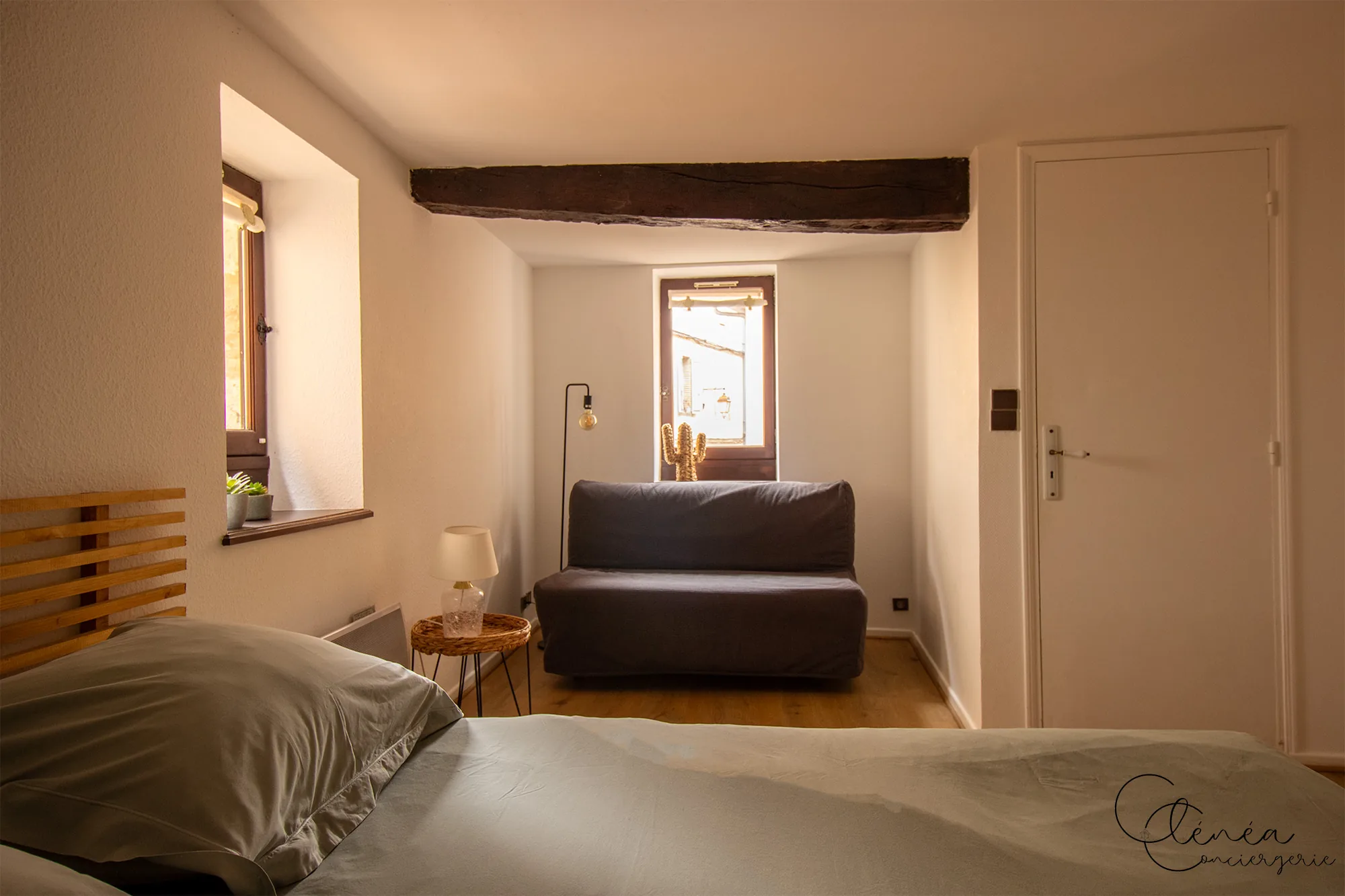 Sous les Toits de Sainte Cécile — Banquette-lit grise placée sous une fenêtre, au fond de la chambre Le Repos du Clocher