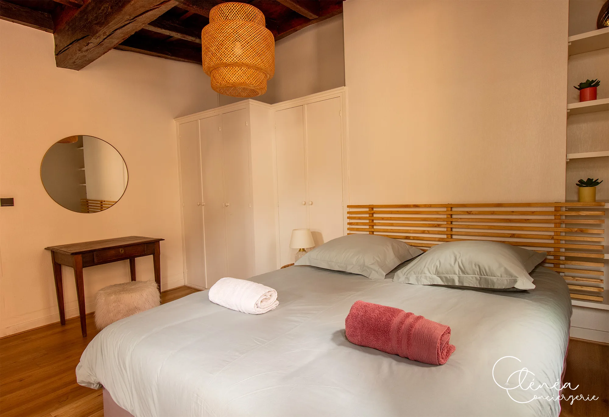 Sous les Toits de Sainte Cécile — Chambre avec grands placards blancs, miroir rond, petite table ancienne et suspension en rotin