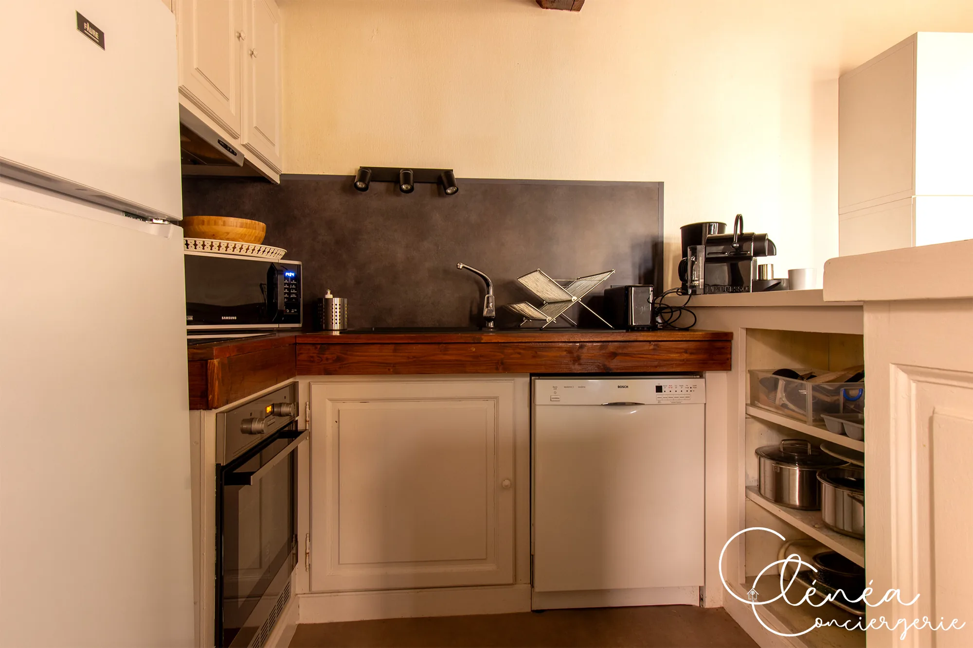 Sous les Toits de Sainte Cécile — Cuisine avec réfrigérateur, four, micro-ondes, plan de travail en bois et rangements ouverts