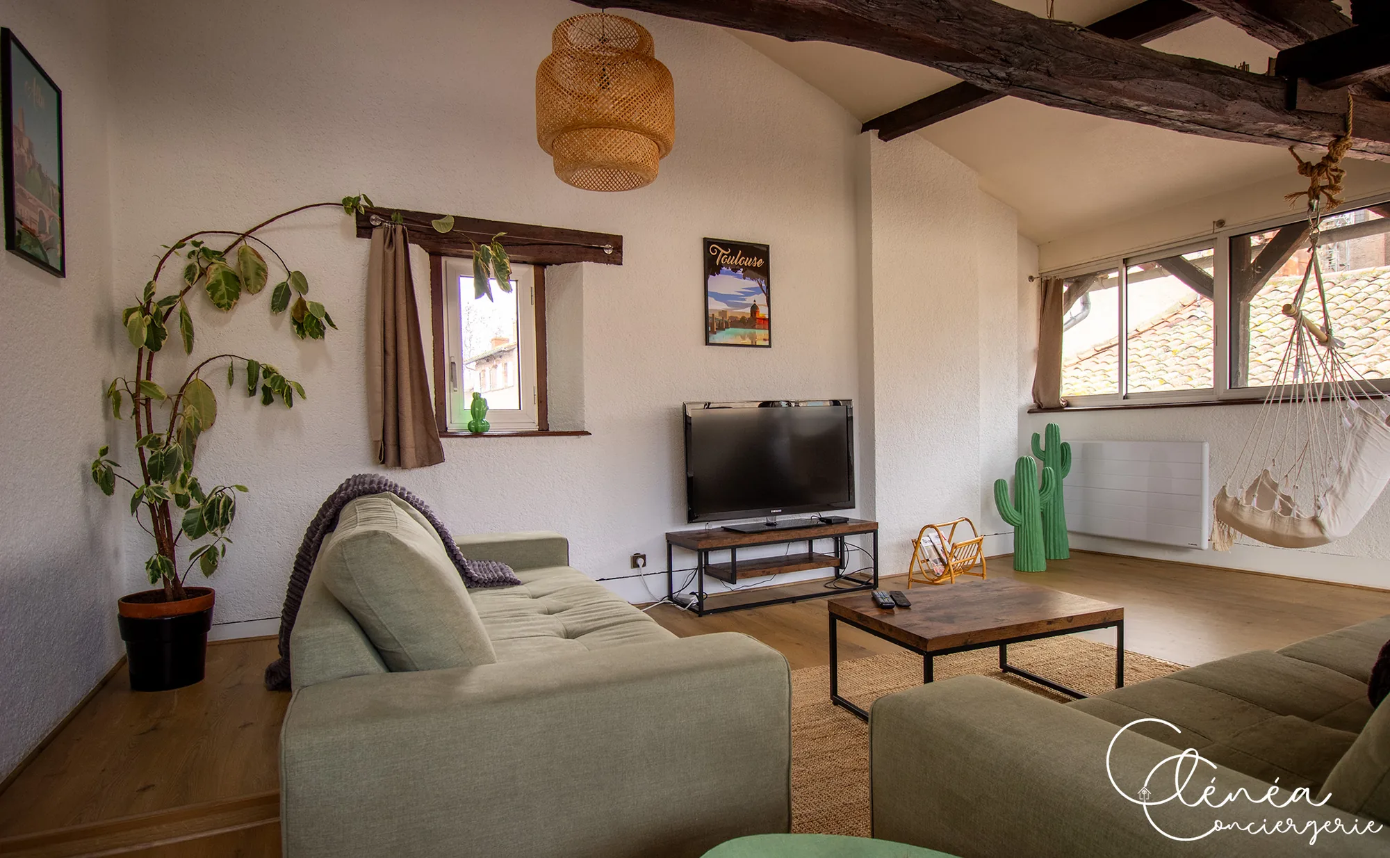 Sous les Toits de Sainte Cécile — Coin télévision du salon avec canapé, table basse et fauteuil suspendu près de la fenêtre