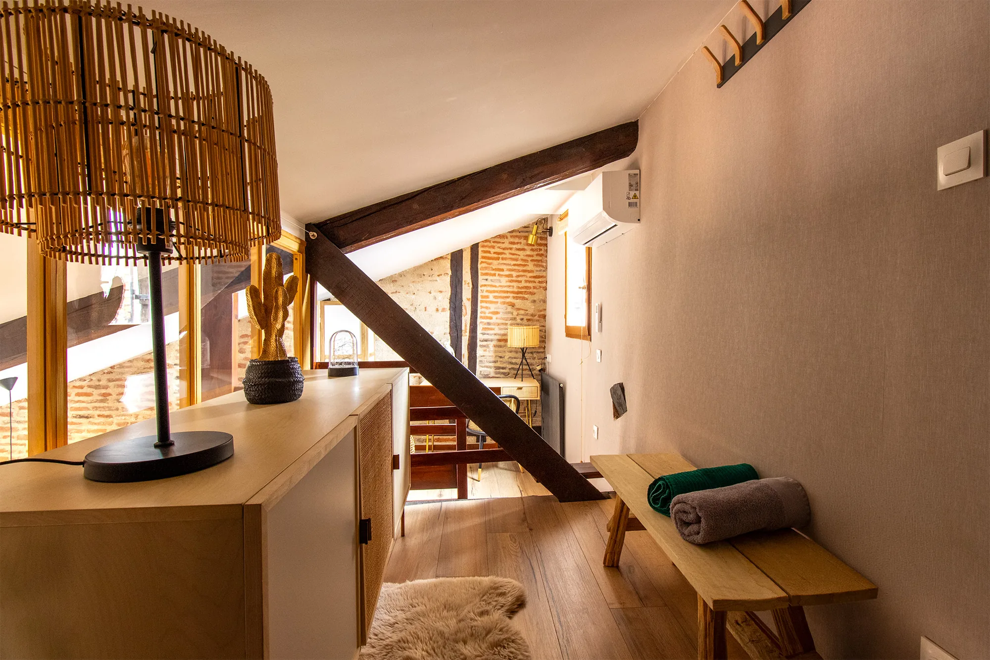 The Nest — Palier de la mezzanine avec commode, banc portant des serviettes et unité de climatisation fixée au mur.