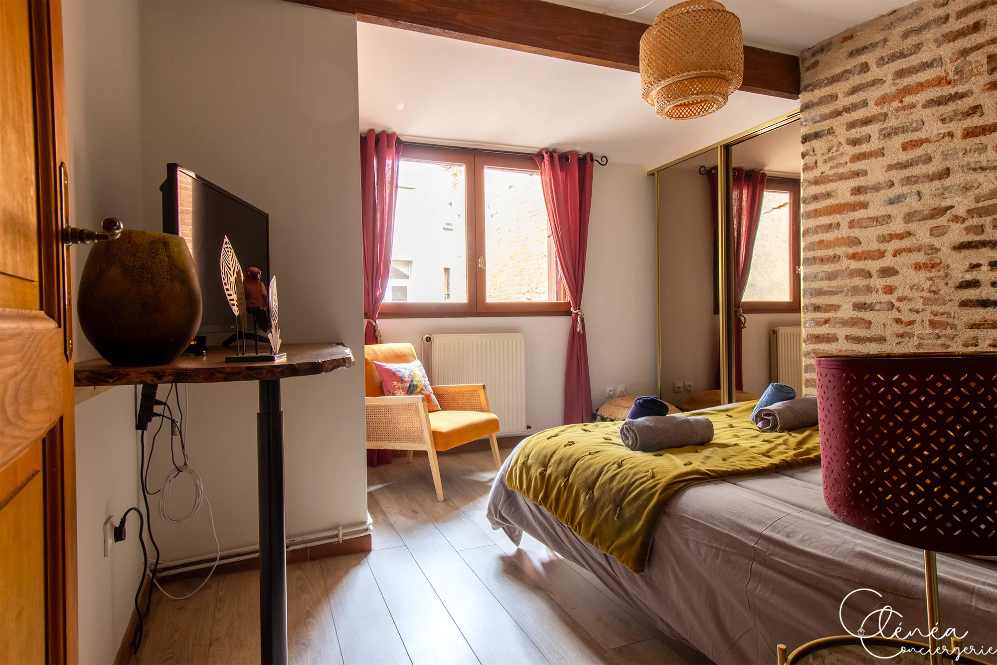 The Nest — Chambre vue depuis l’entrée, avec télévision, fenêtre habillée de rideaux rouges, fauteuil orange et placard miroir.