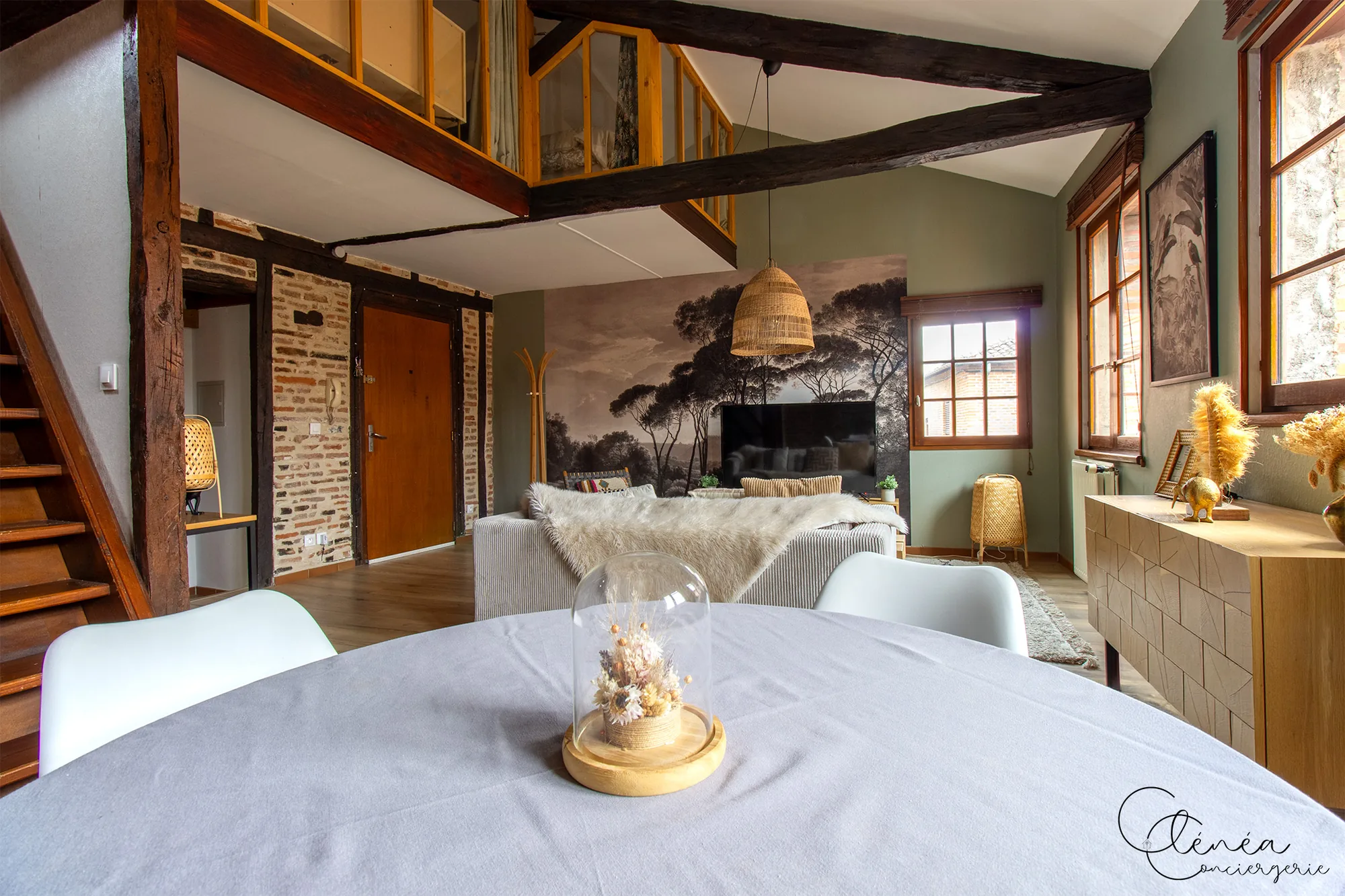 The Nest — Vue depuis la table à manger sur le salon, l’escalier en bois et la mezzanine vitrée qui surplombe la pièce de vie.