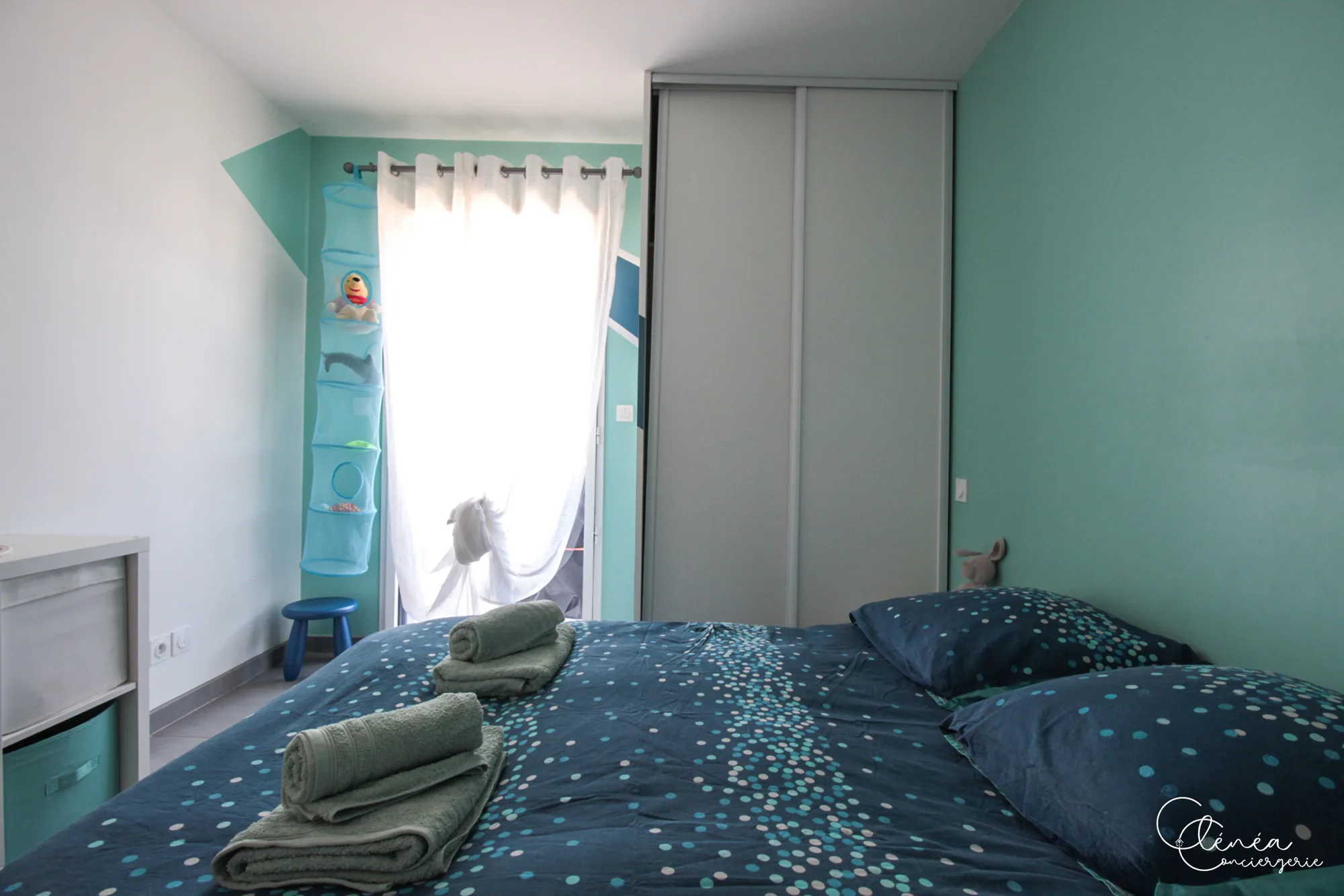 Urban Jungle — Chambre aux murs turquoise avec lit double, housse de couette bleue à pois et placard à portes coulissantes.