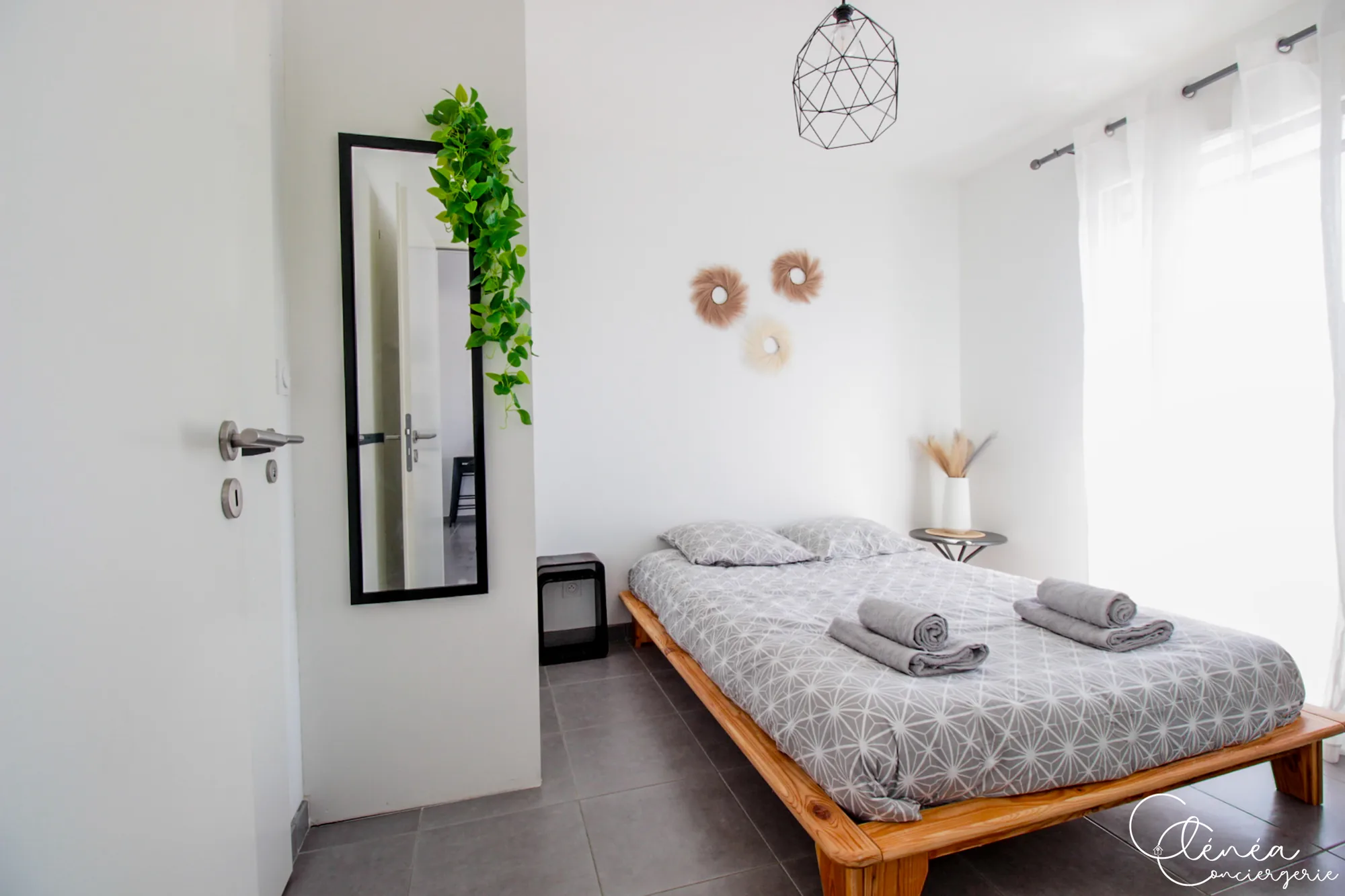Urban Jungle — Chambre avec lit double sur cadre en bois, grand miroir mural encadré de noir et plante retombante.