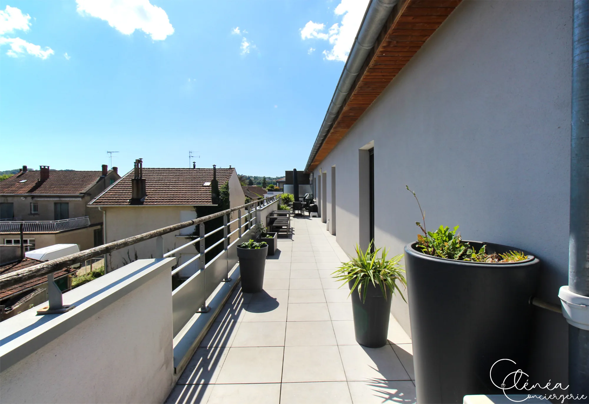 Urban Jungle — Longue terrasse carrelée bordée de pots de plantes, longeant la façade de l’appartement.