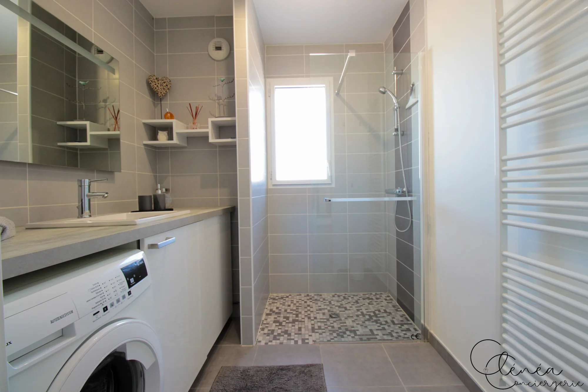 Urban Jungle — Salle de bain avec douche à l’italienne au sol en mosaïque, meuble vasque et lave-linge encastré.