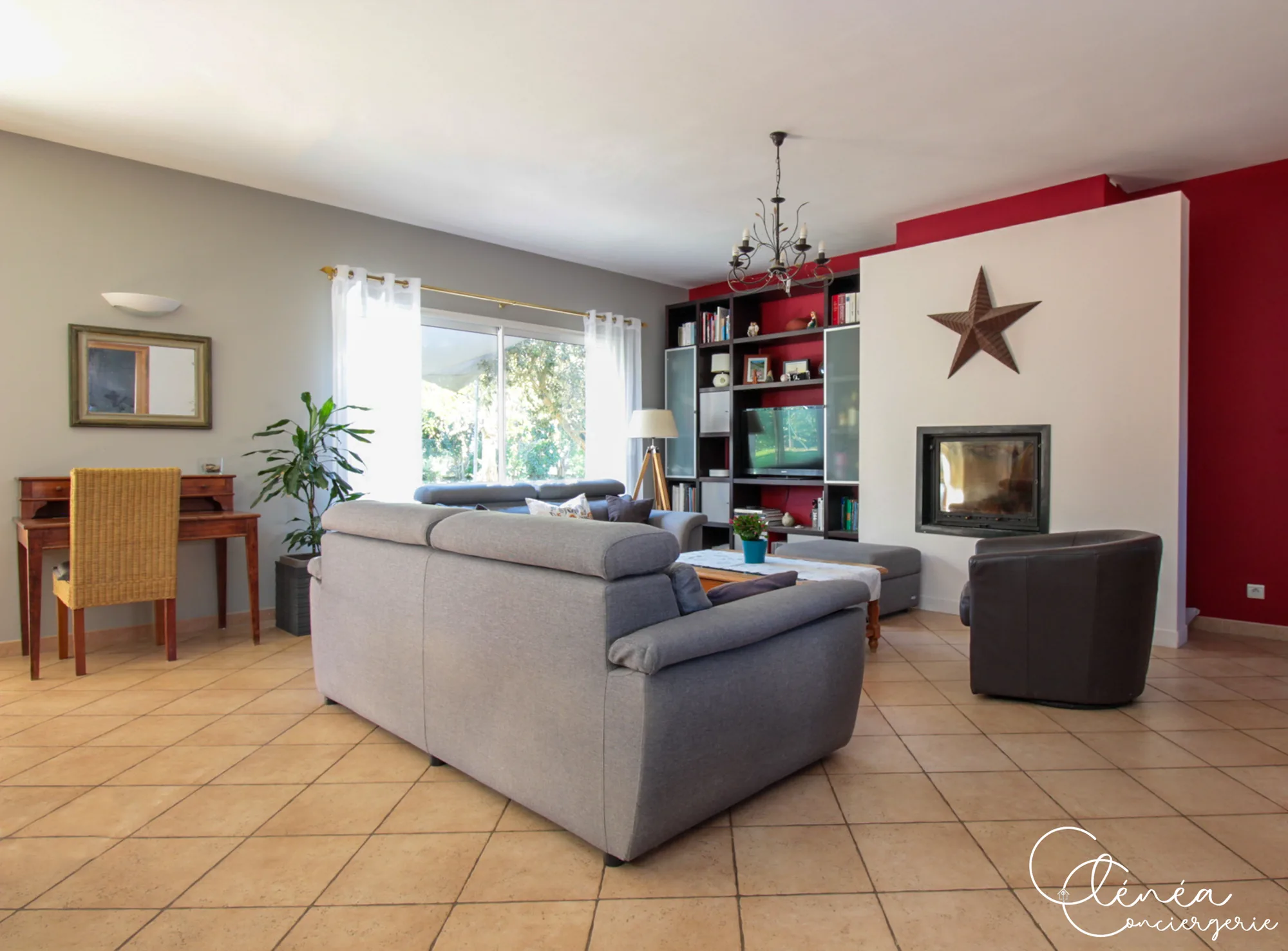 Villa Chanoine — Le salon avec ses canapés gris, sa cheminée insert et son mur rouge, ouvert sur une large baie vitrée.