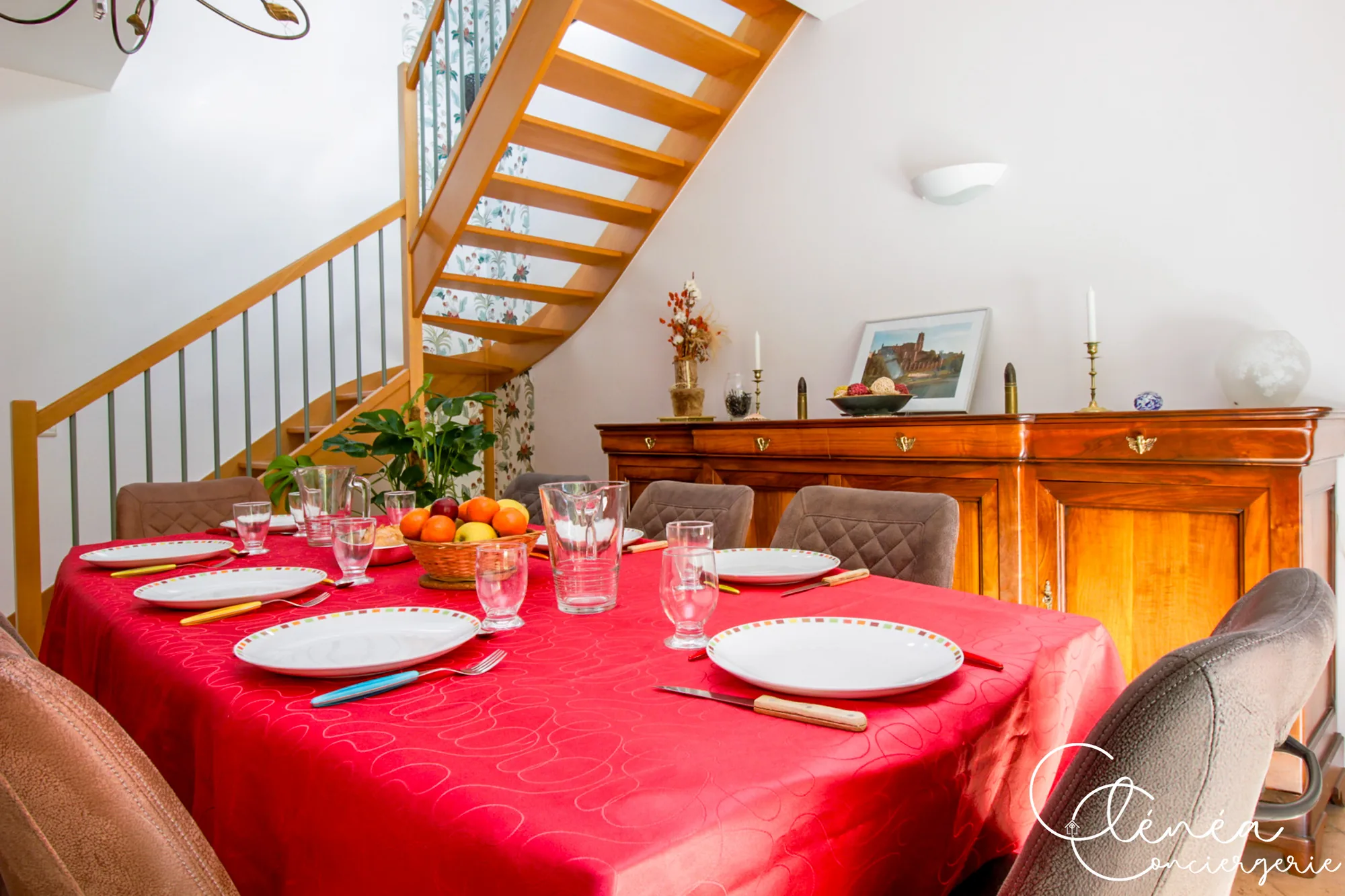 Villa Chanoine — La table de la salle à manger dressée avec assiettes et verres, au pied de l'escalier en bois.