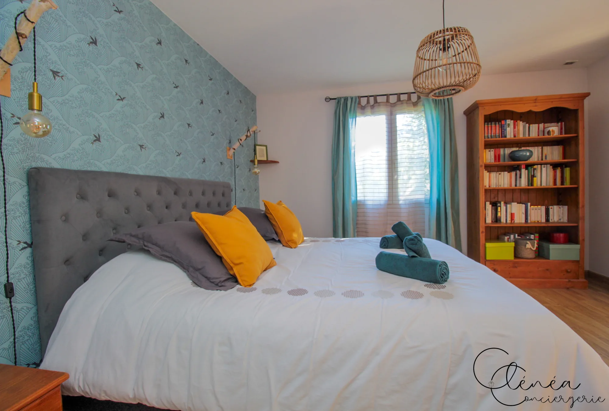 Villa Chanoine — La chambre 1 avec son lit King size, sa tête de lit capitonnée, son papier peint à motif de vagues et sa bibliothèque.