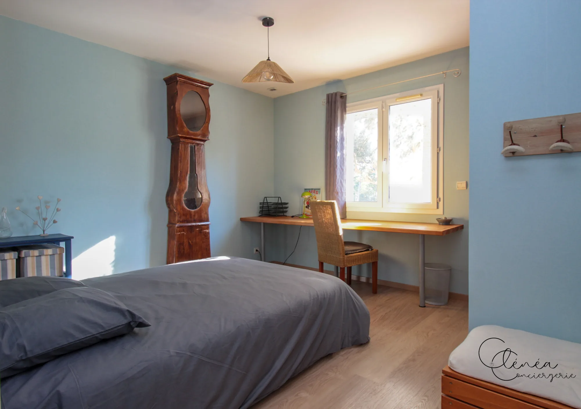 Villa Chanoine — Une chambre aux murs bleu clair avec son lit double, une horloge comtoise ancienne et un plan de bureau sous la fenêtre.