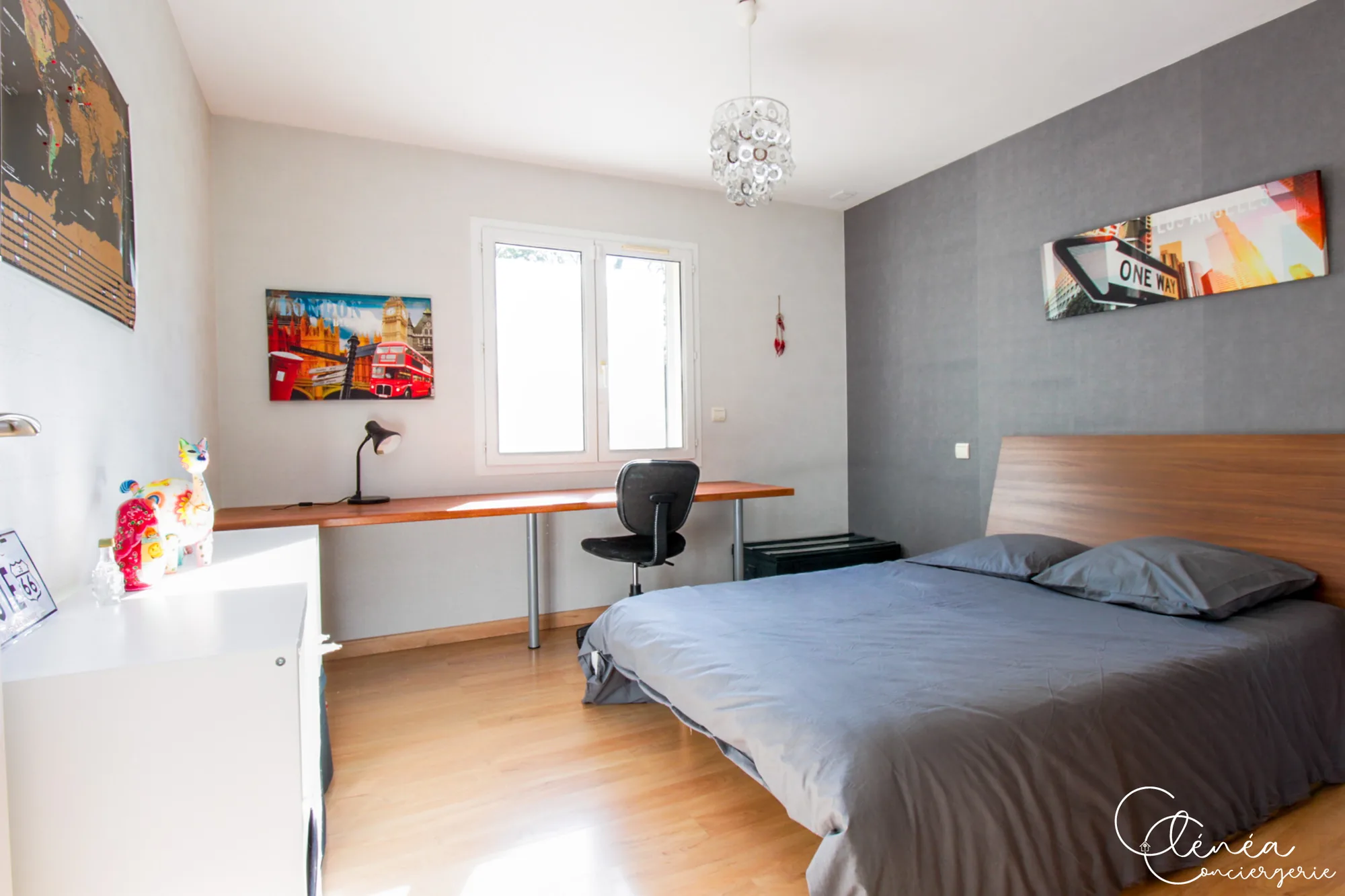 Villa Chanoine — Une chambre aux murs gris avec lit double, long plan de bureau sous la fenêtre et affiches de voyage.
