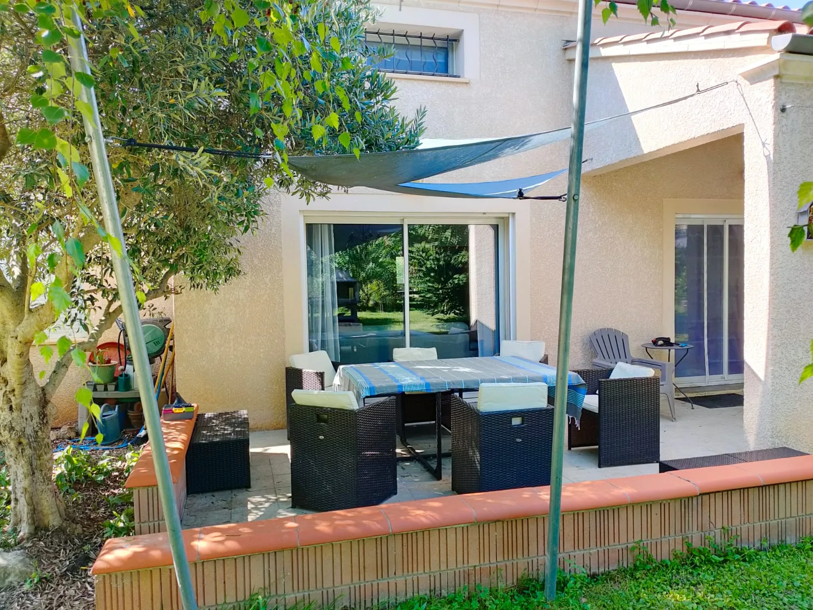 Villa Chanoine — La terrasse aménagée avec son salon de jardin en résine tressée et sa voile d'ombrage, contre la façade de la maison.